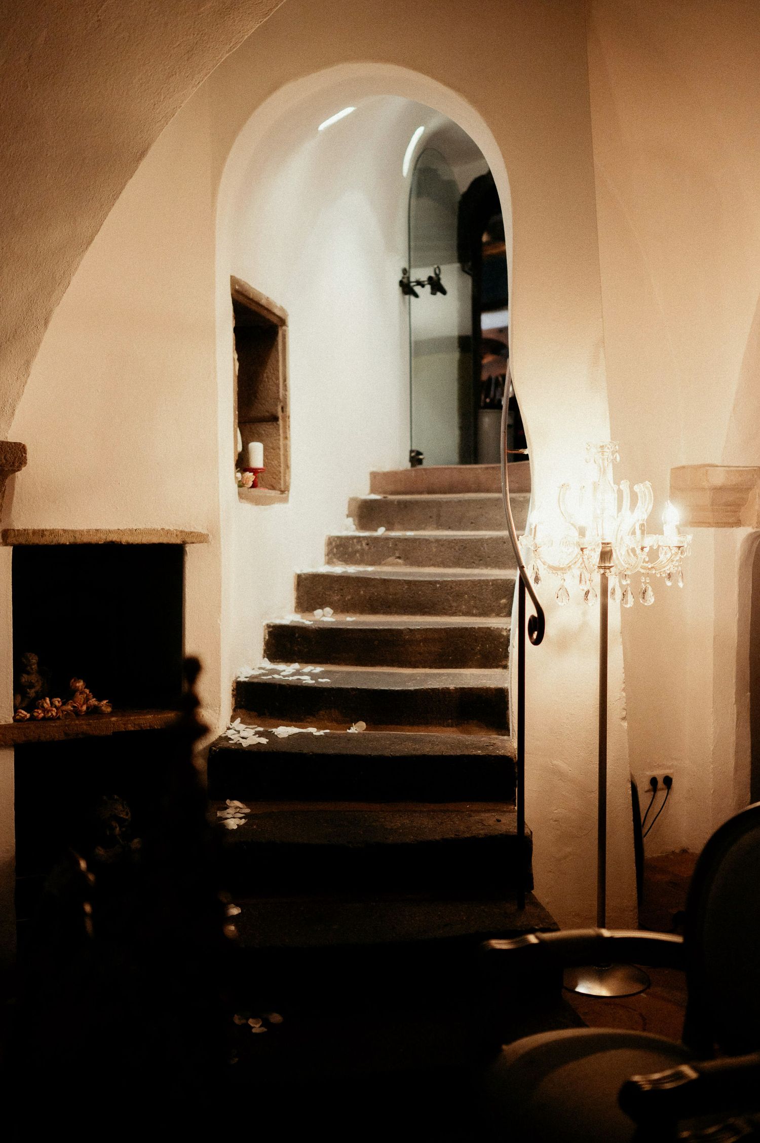 Dimly lit stone staircase with arched walls and hanging chandeliers creates moody atmosphere.
