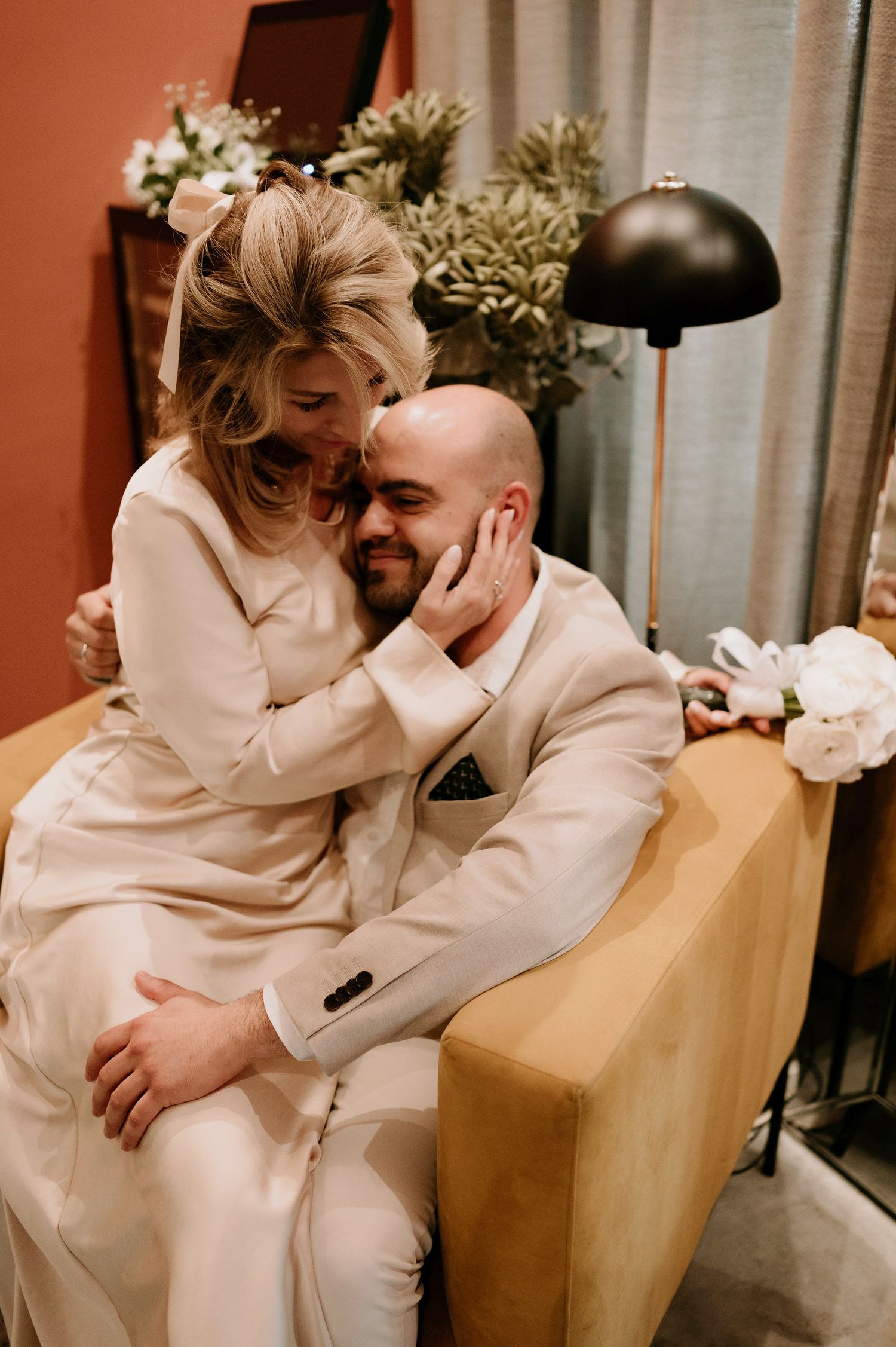 A couple in matching white outfits share a romantic moment on a tan couch.