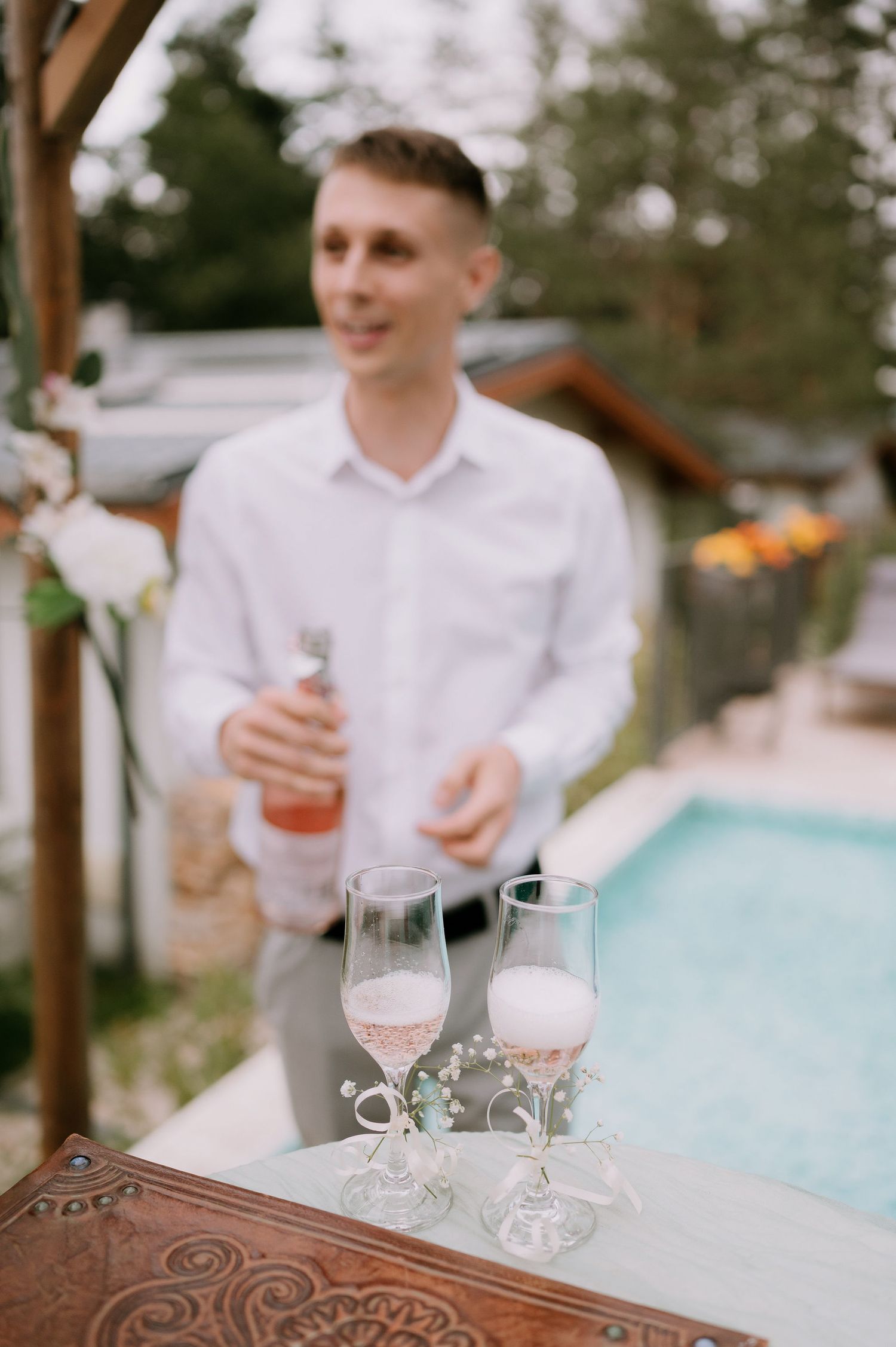 Outdoor setting with champagne glasses on table and pool in background.