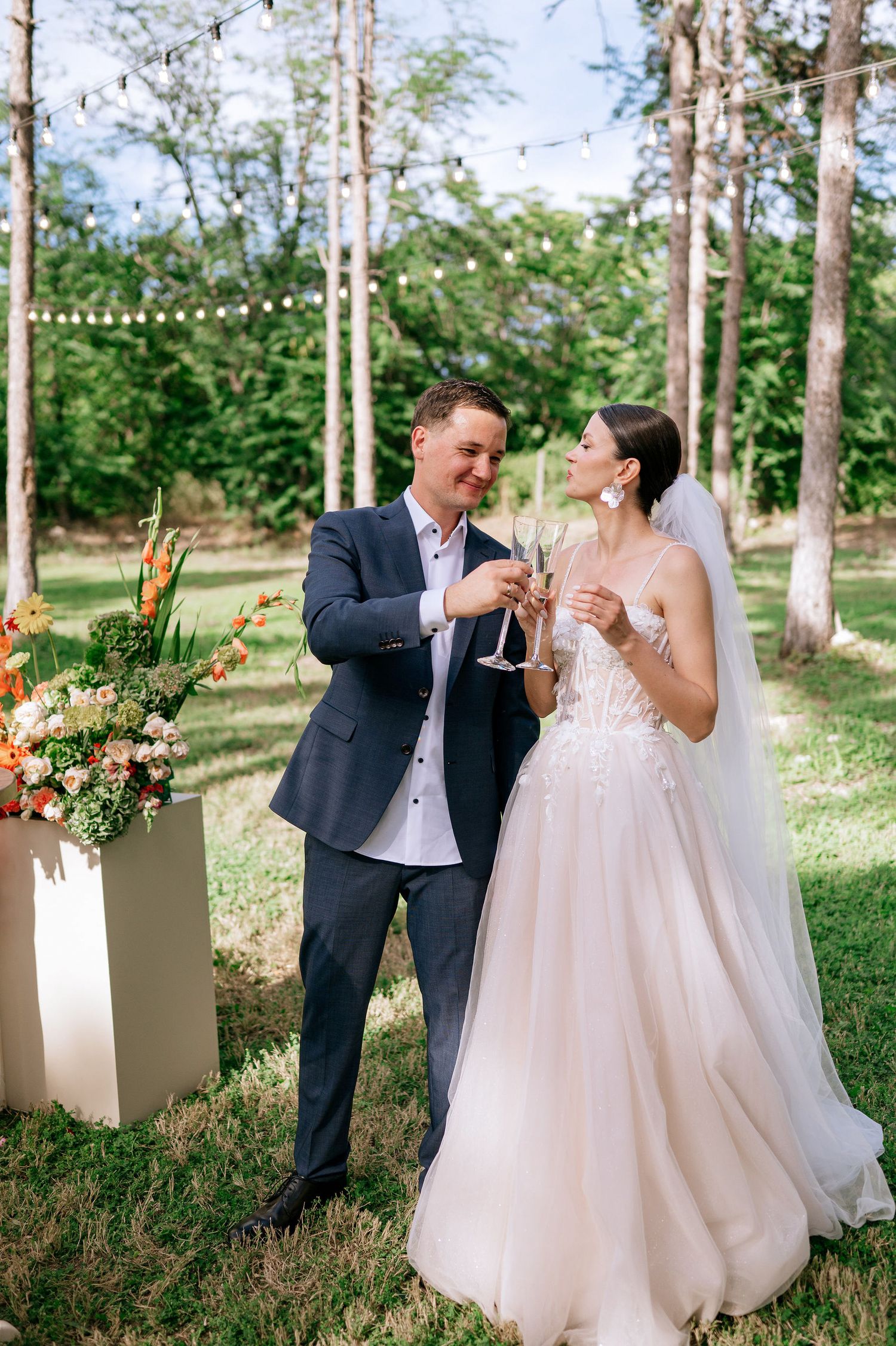 A joyful wedding couple dances and celebrates among pine trees and white floral arrangements.
