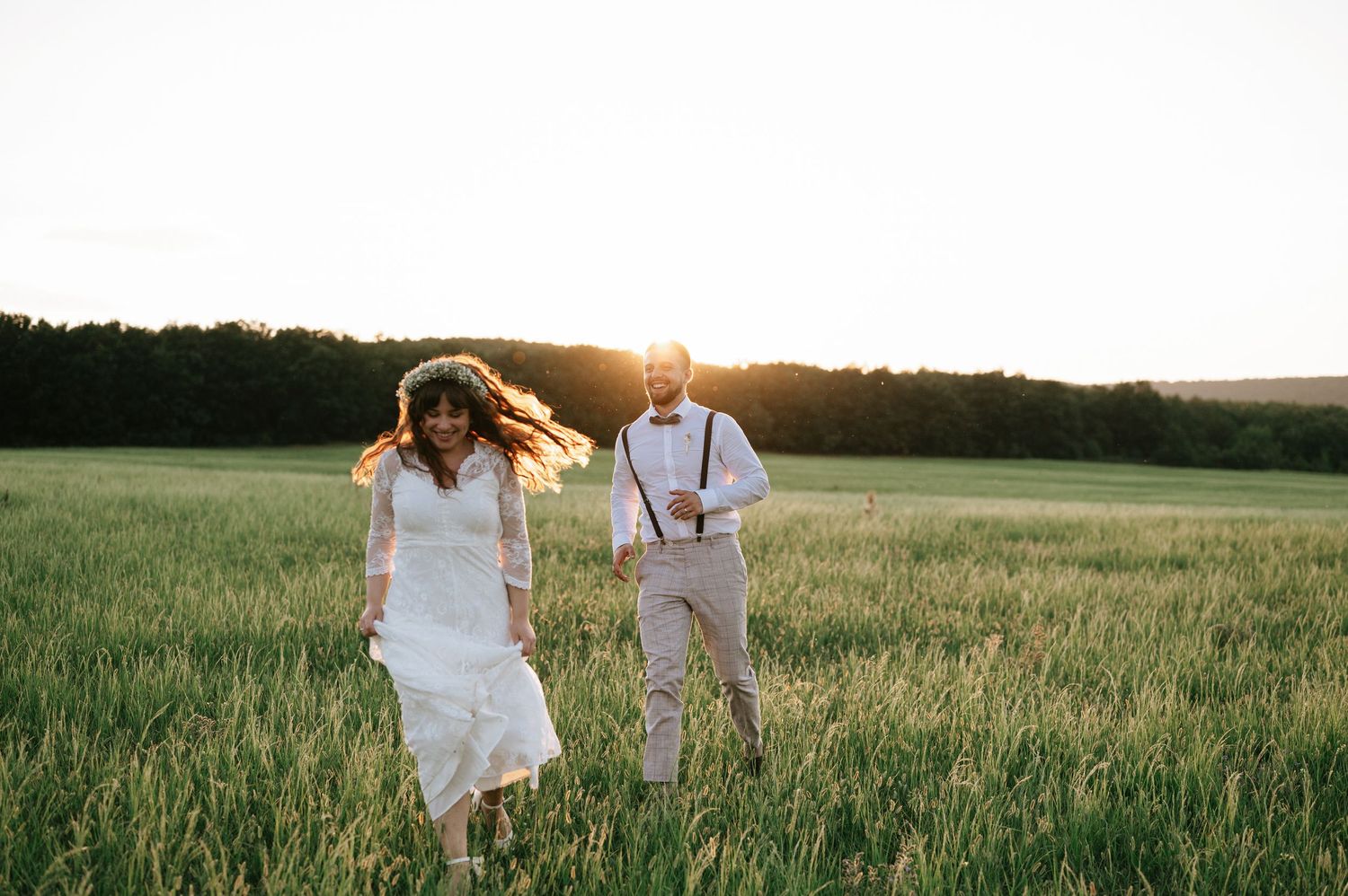 A couple runs playfully through a sunlit meadow at golden hour.