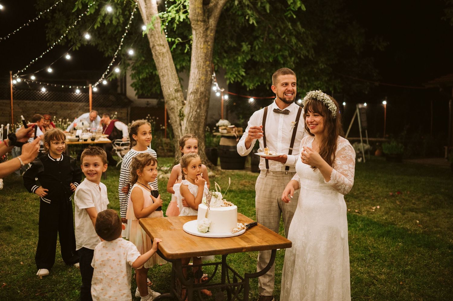 Outdoor wedding reception under string lights with tables and guests.