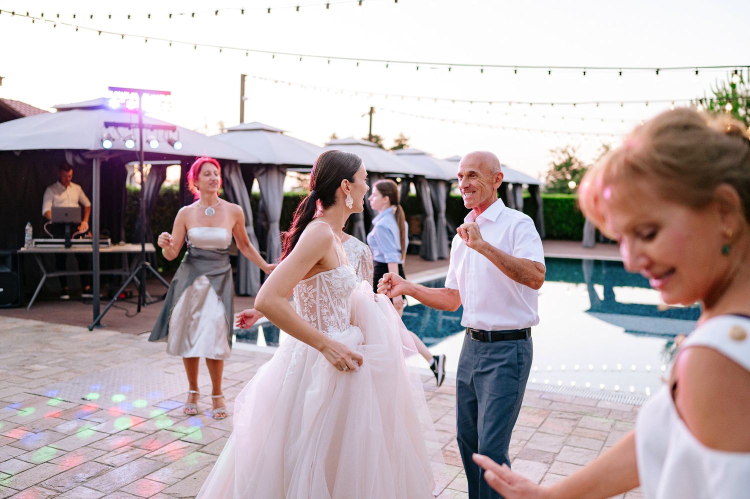 Wedding guests dancing on a patio under string lights at dusk.