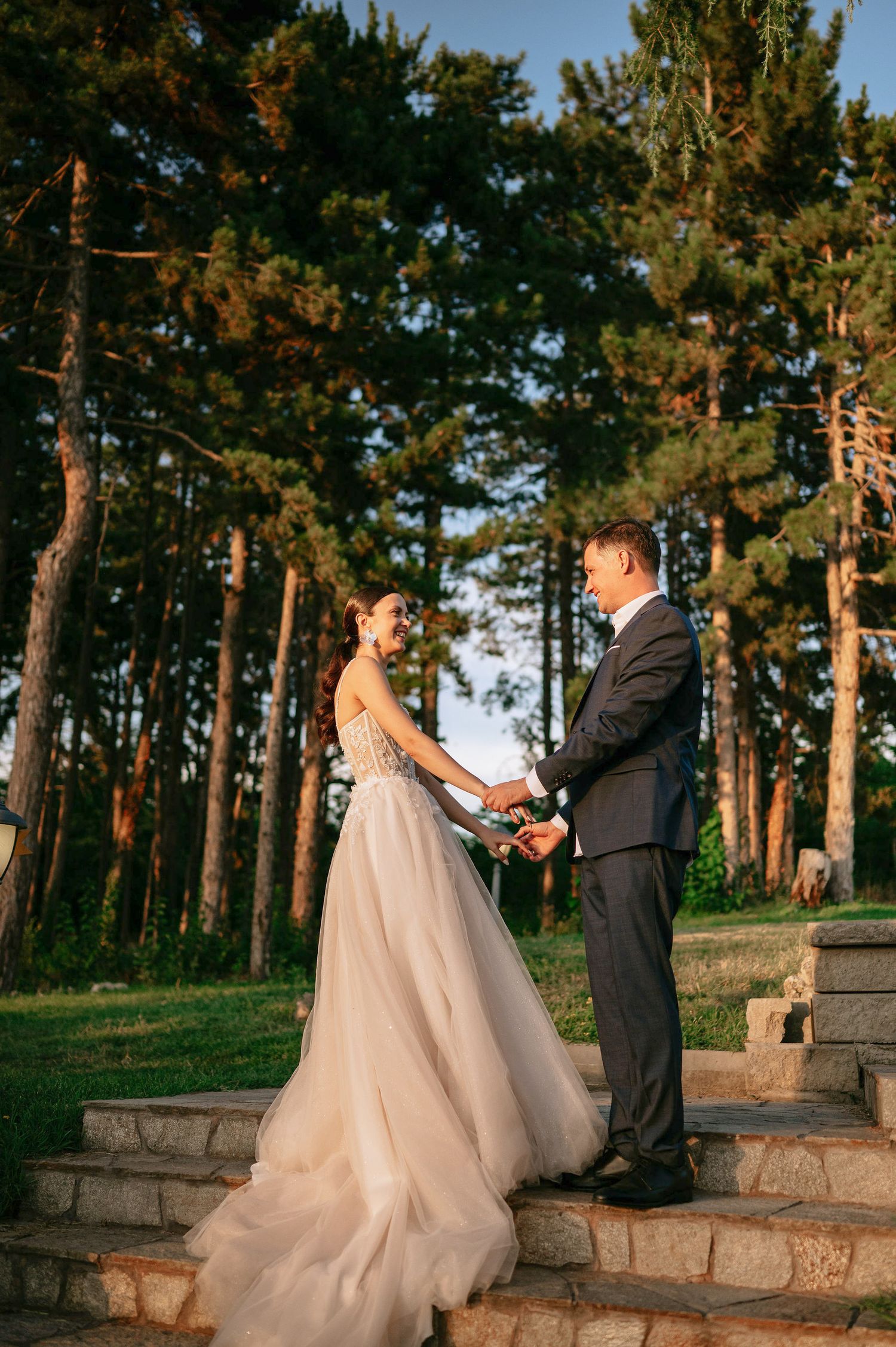 Wedding couple dancing and twirling on stone steps in a pine forest setting.