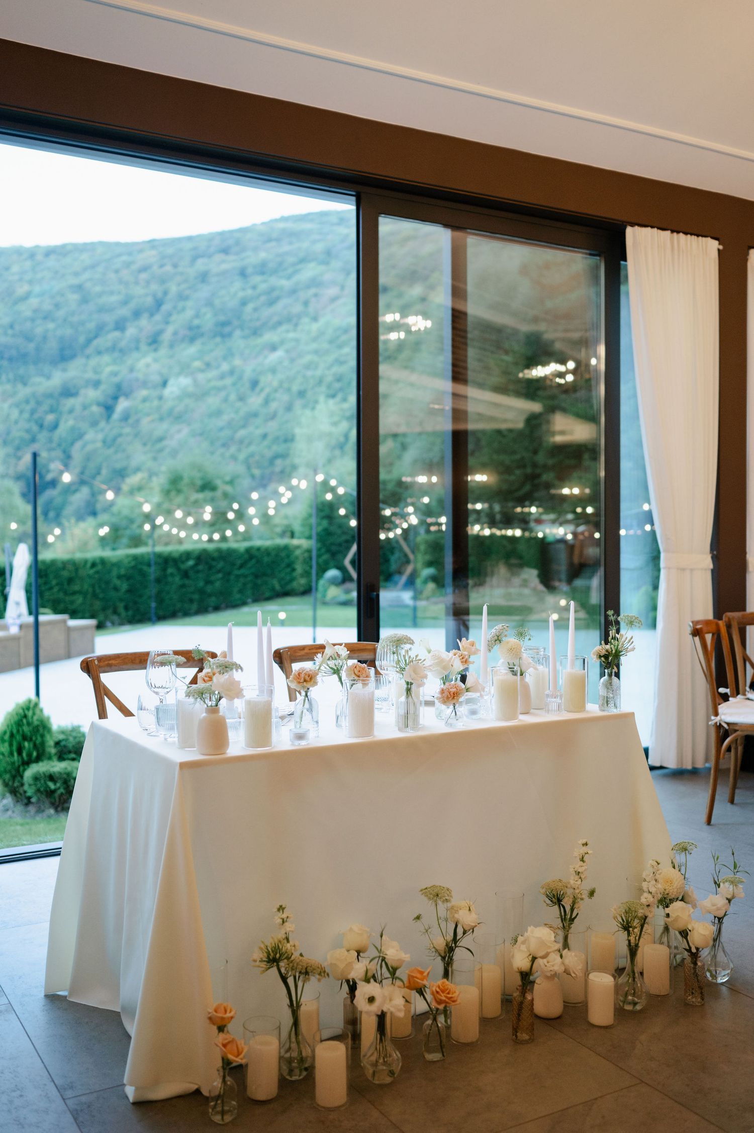 Modern reception venue with white-clothed tables and mountain vistas through floor-to-ceiling windows.