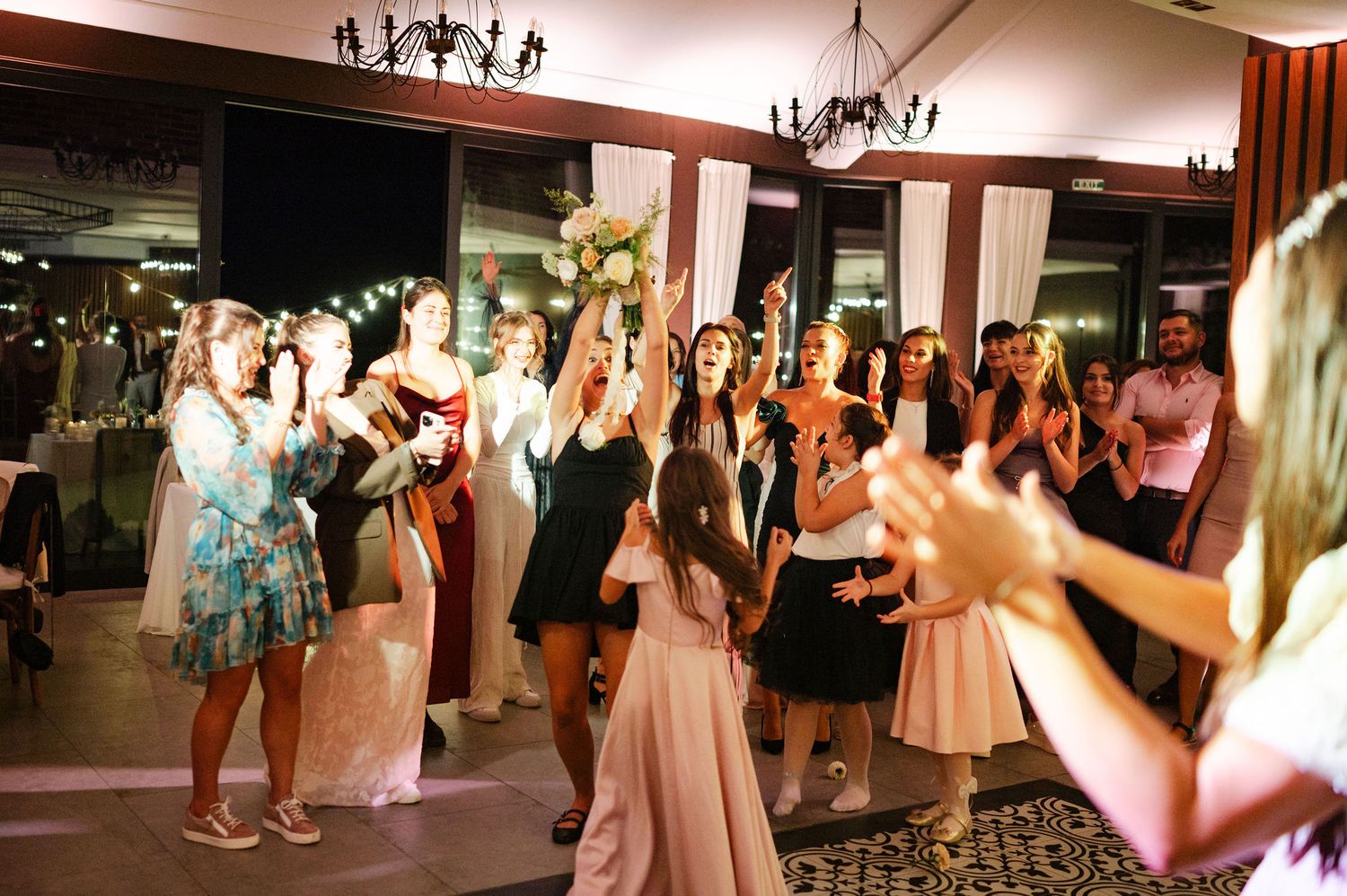 Guests in colorful dresses gather on a dance floor during a celebratory event.