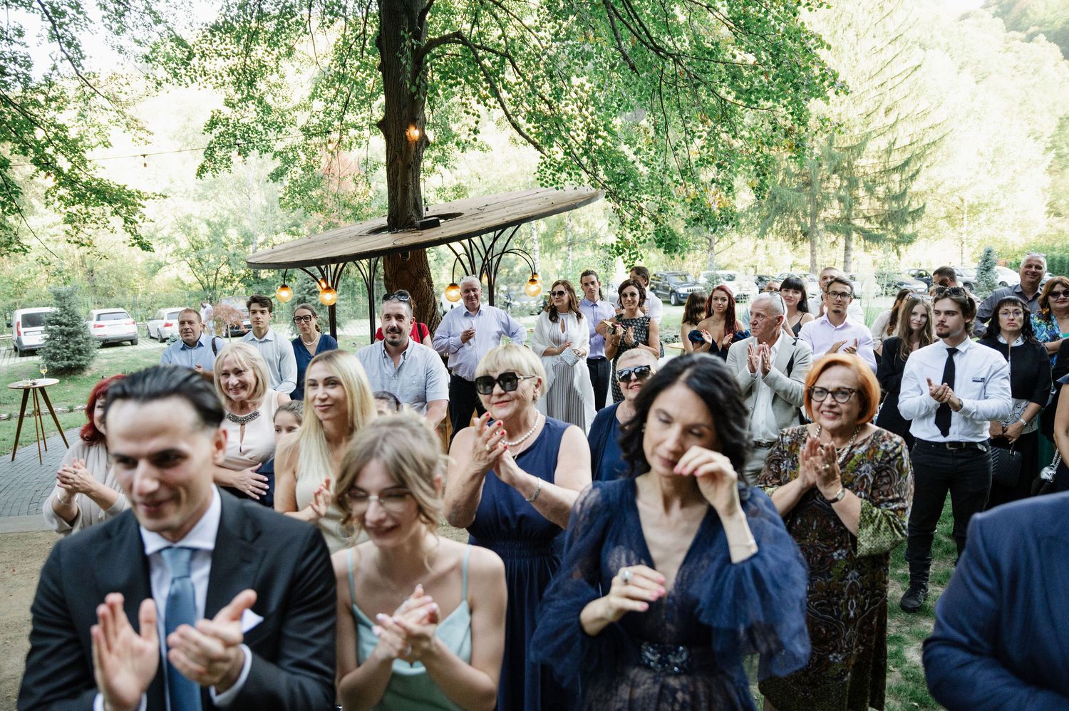 Wedding guests cheer and celebrate during an outdoor forest ceremony.