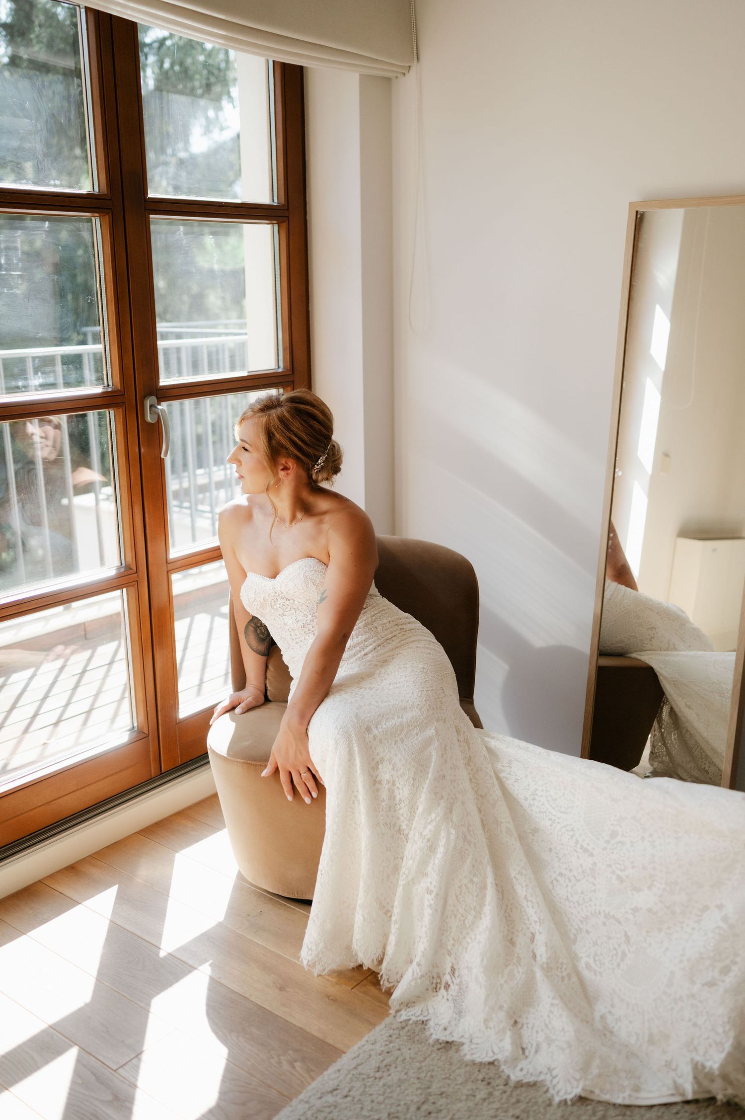 A white wedding dress is illuminated by natural light streaming through wooden-framed windows.
