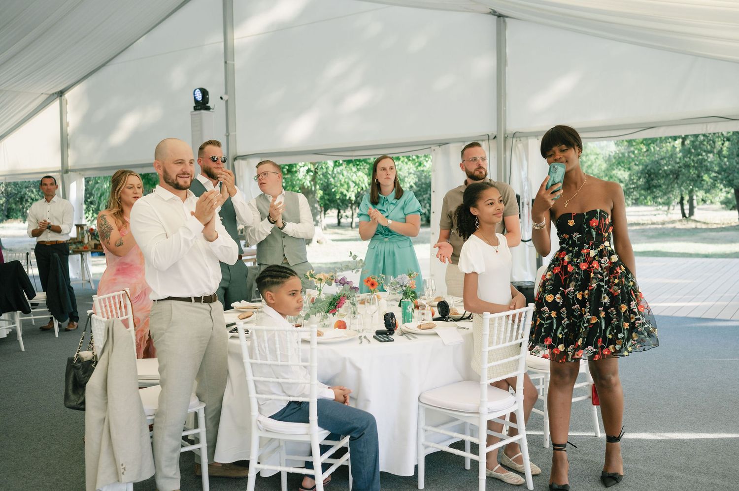 Wedding reception guests seated at tables under a white tent celebrate with raised glasses.
