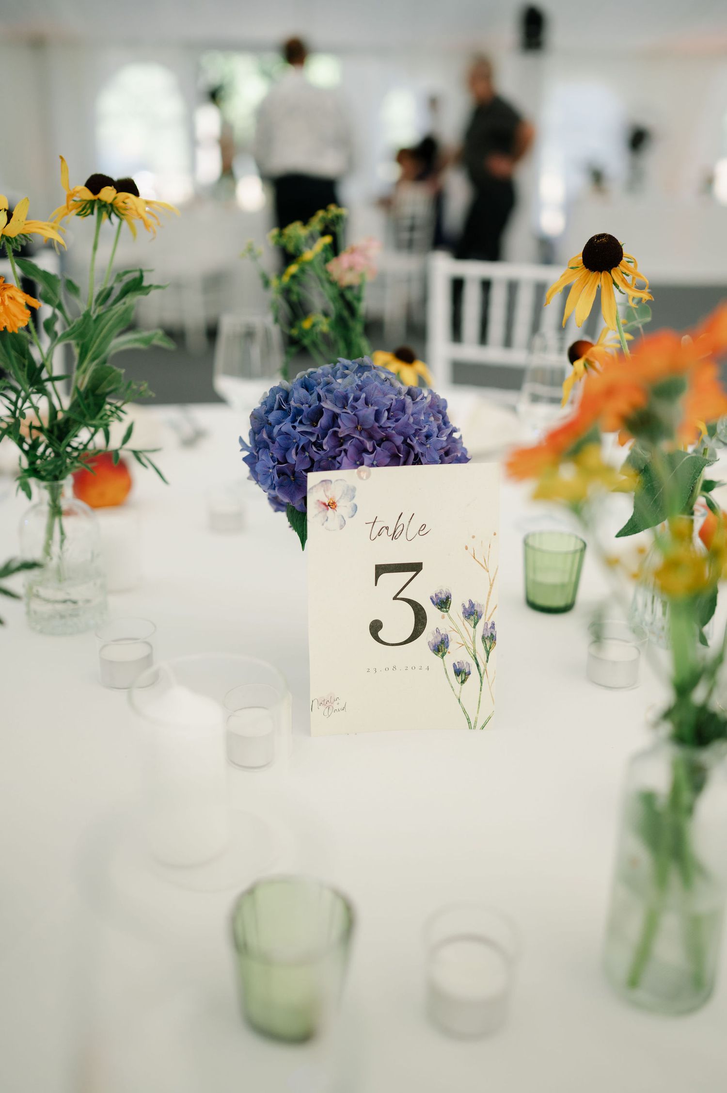 Elegant table settings with mason jar centerpieces filled with wildflowers and sunflowers.