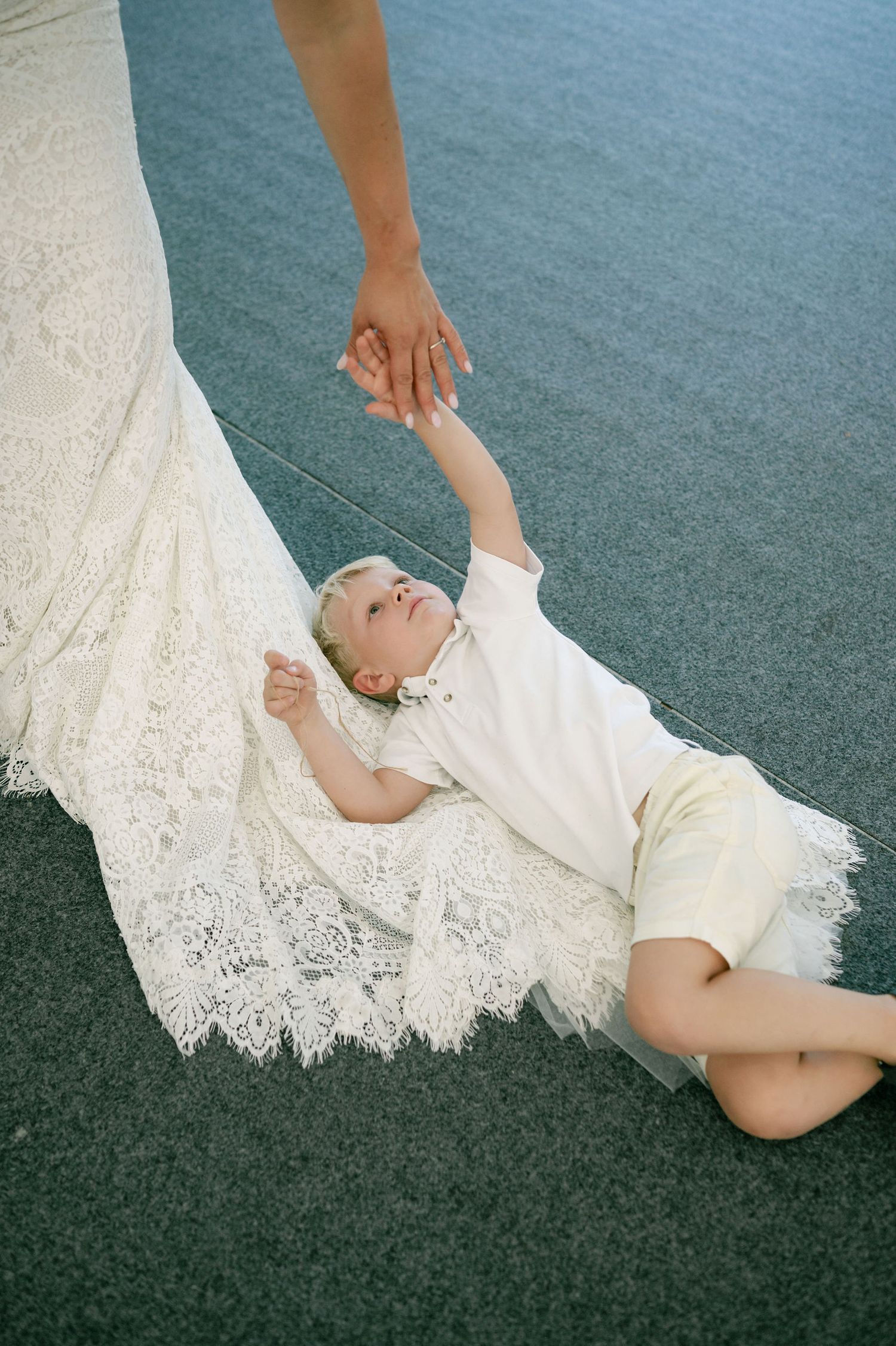 A person in white clothing reclining on gray carpet with lace fabric trailing beside them.