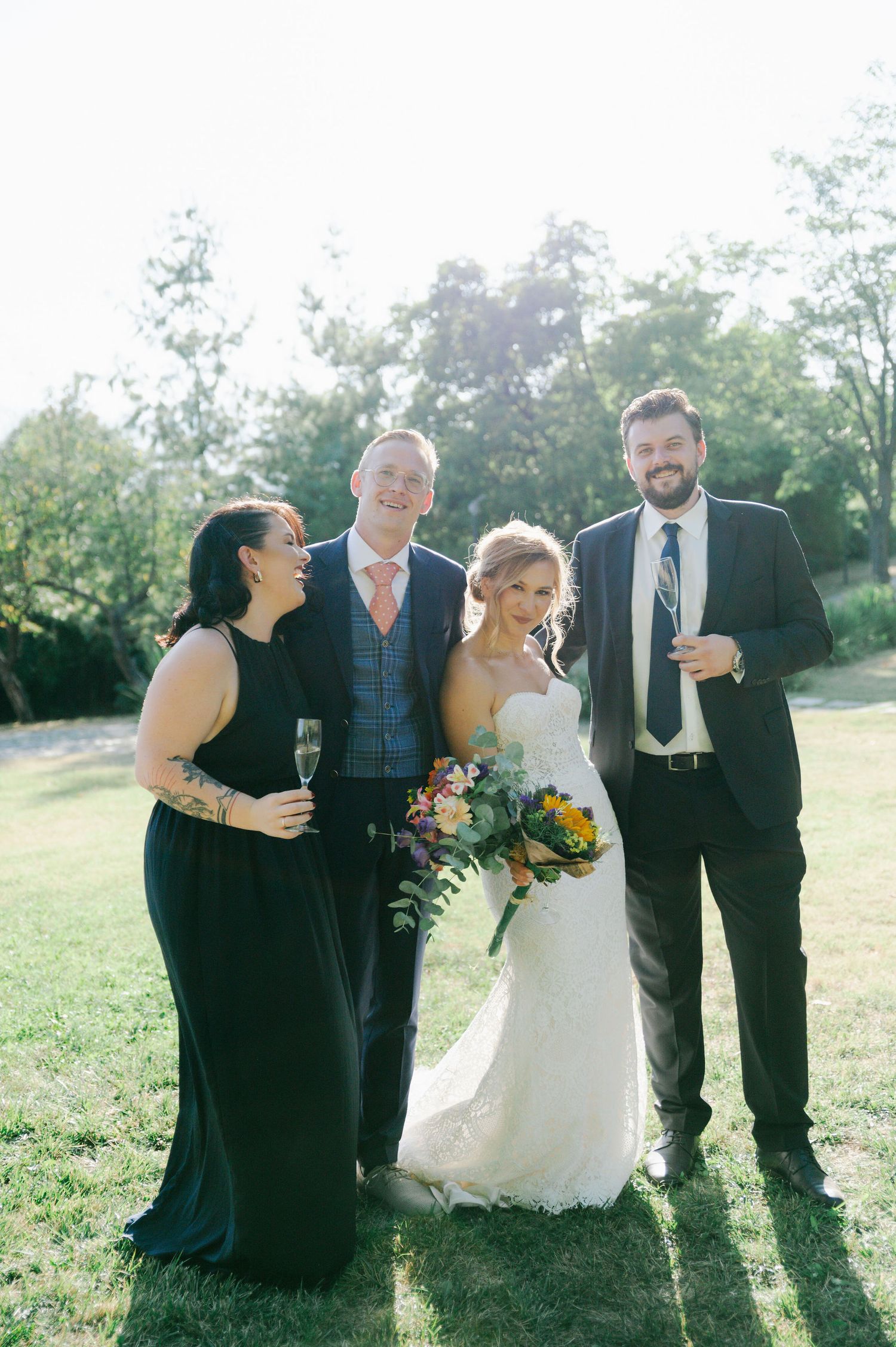 Wedding party stands together on sunny hillside sharing joyful moments.