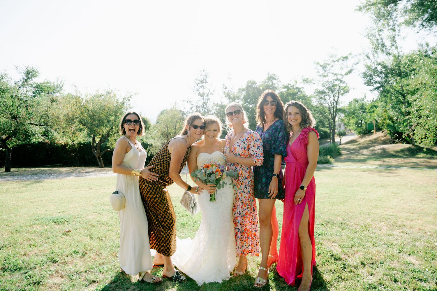 Wedding party poses for group photos in a scenic outdoor setting with natural greenery.
