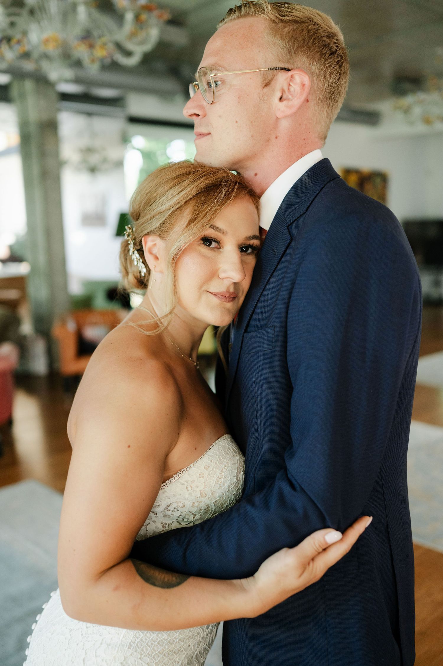 Sweet wedding moment captured in natural light with elegant chandelier in background.