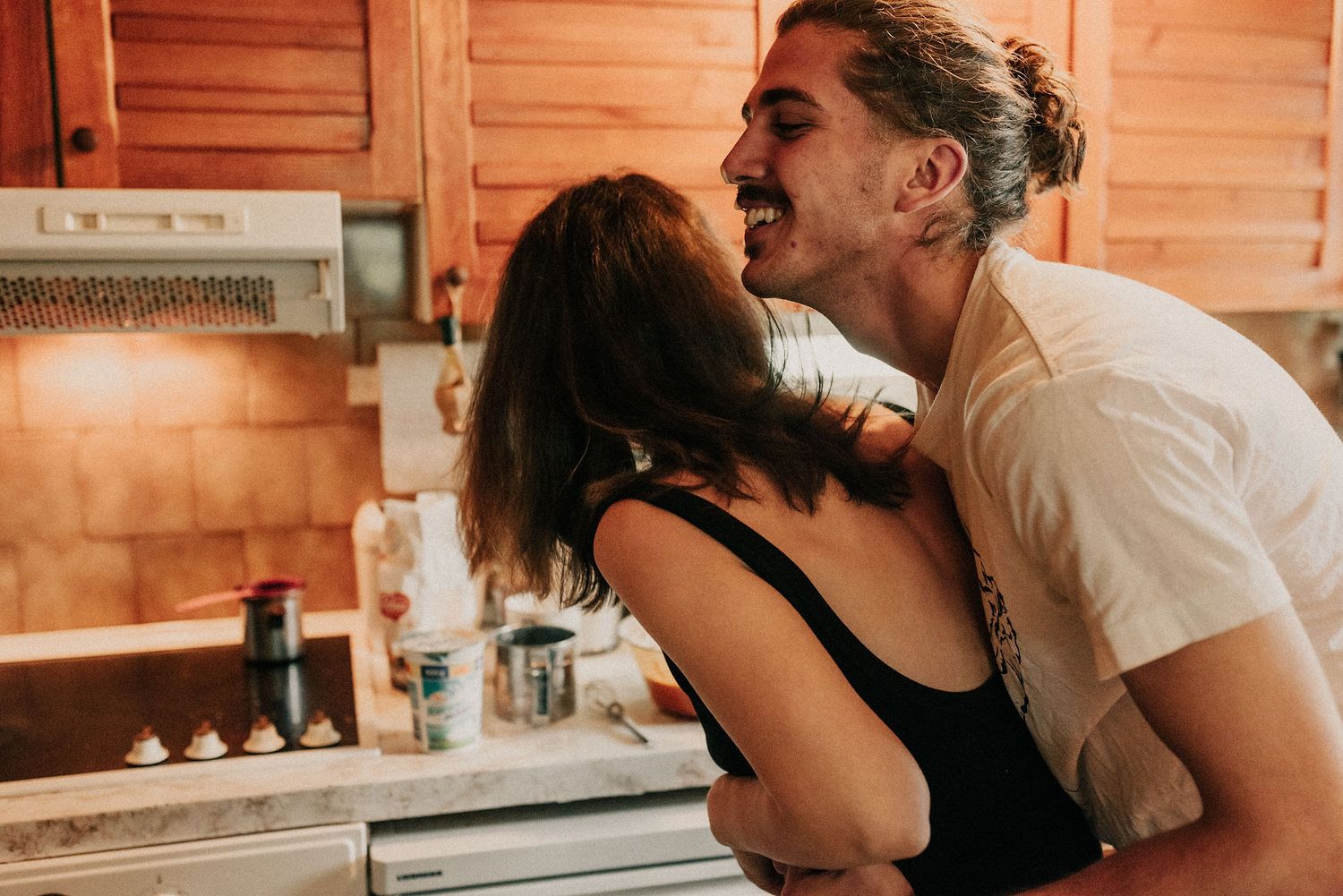 Two people share an intimate moment in a wooden cabin kitchen setting while preparing food together.
