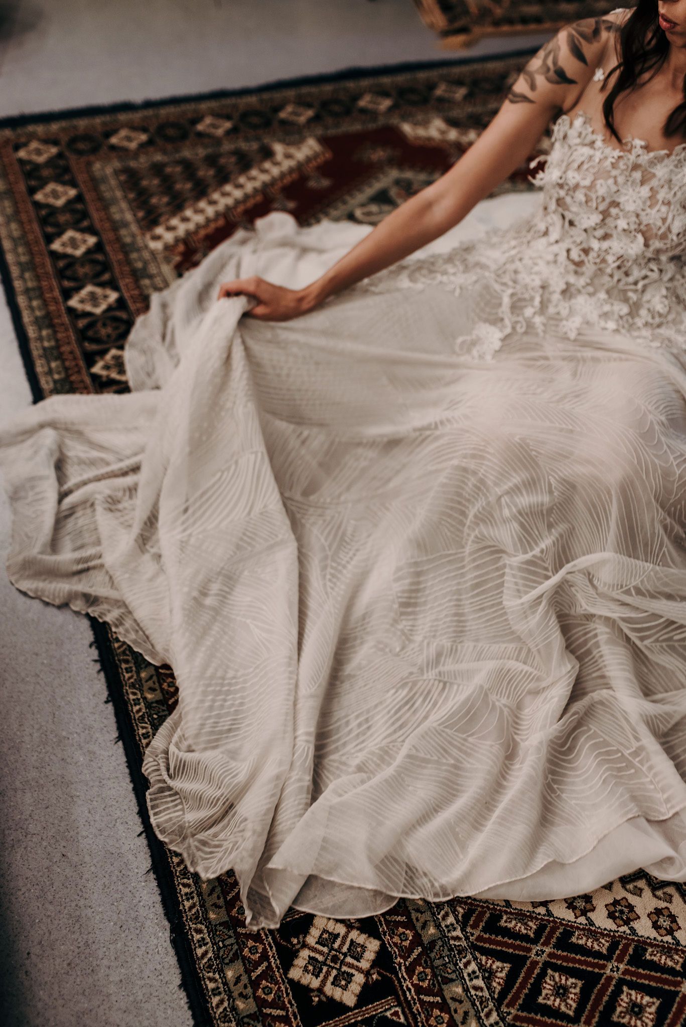 Overhead view of white wedding dress with textured fabric spread across patterned carpet.