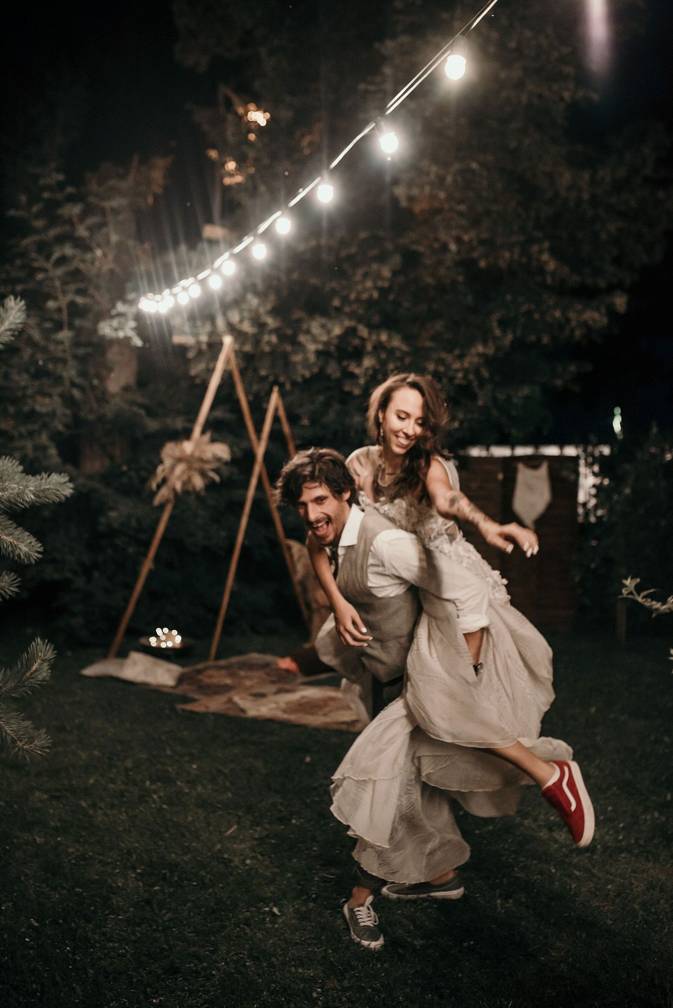 Couple on a swing at night under string lights sharing romantic moments in a garden setting.