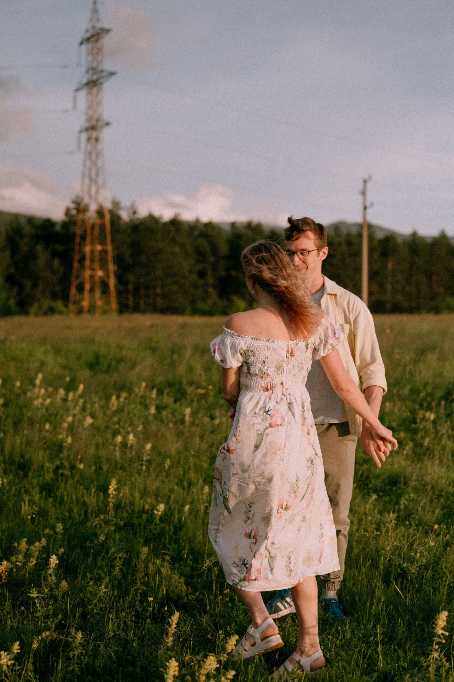 A romantic moment between two people in a grassy field with power lines in the background.