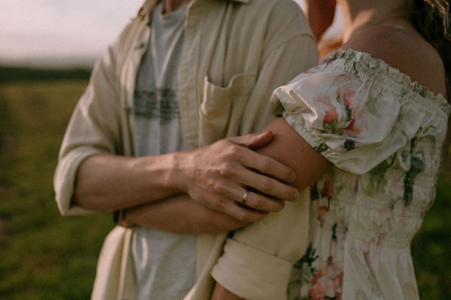 Couple in casual attire embracing in countryside setting.