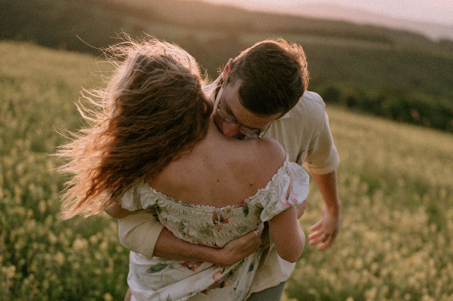 Playful couple embracing in a field of yellow flowers during golden hour.