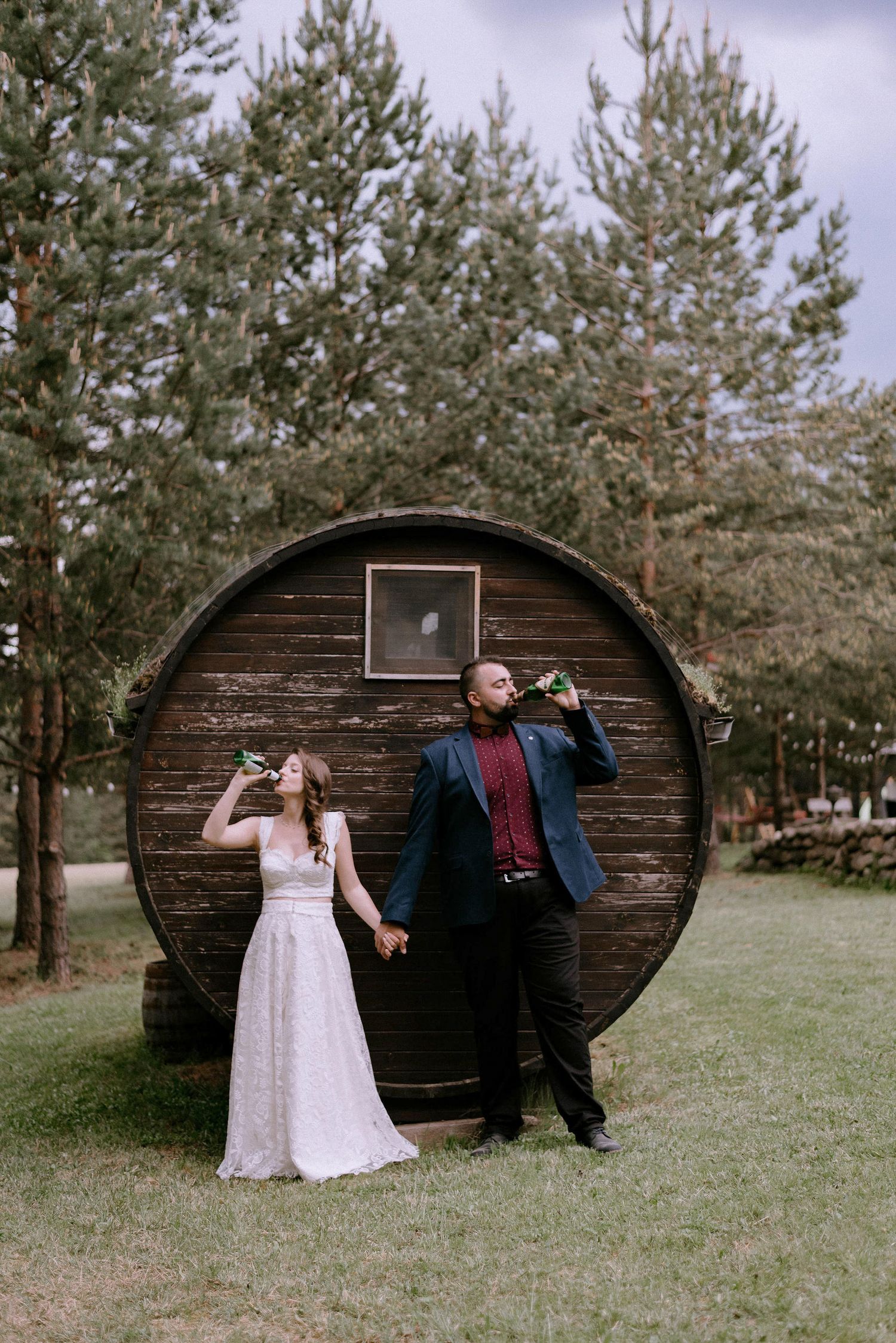 A couple poses playfully in front of a curved wooden structure in a forest setting.