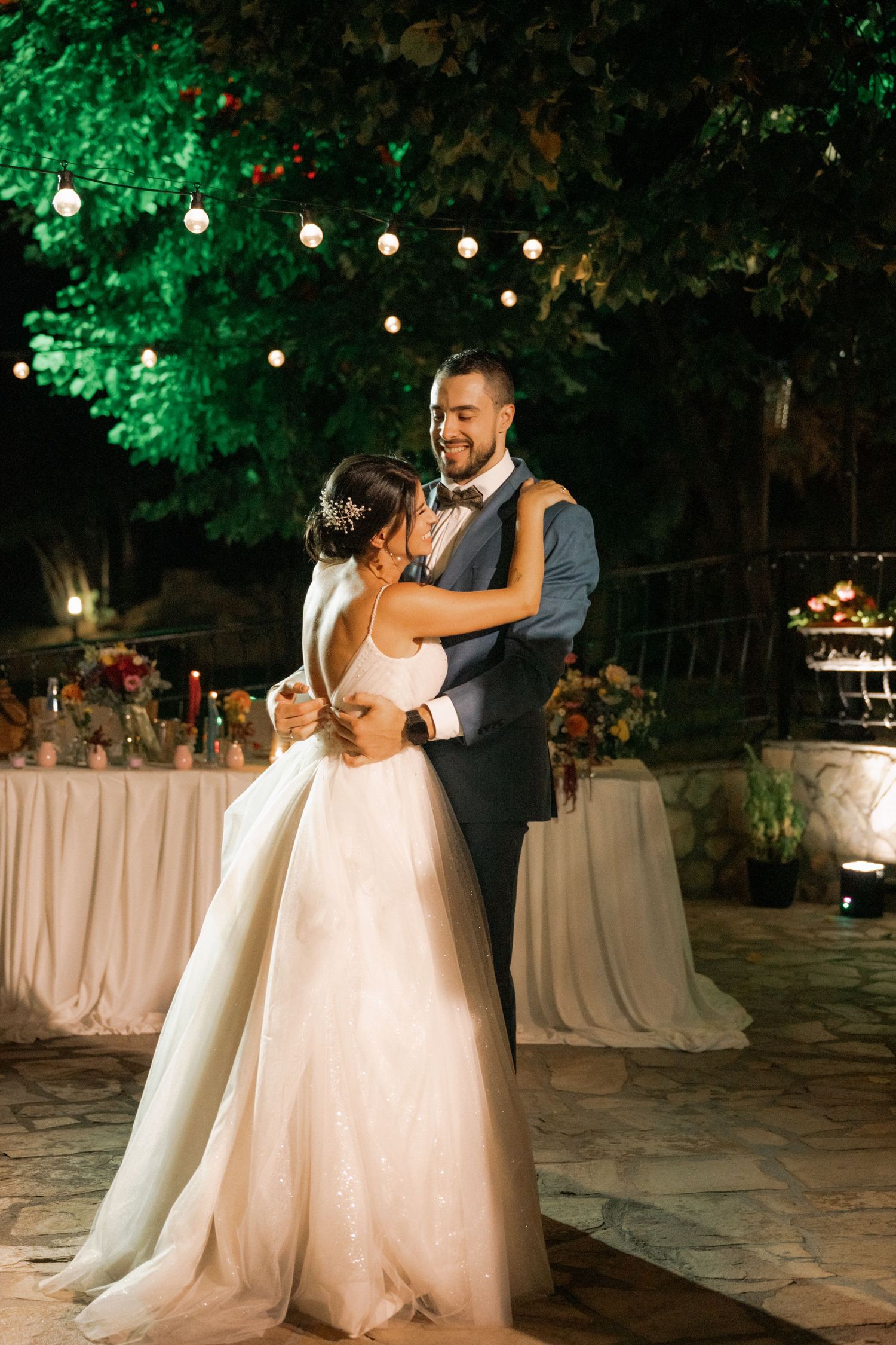 Newlyweds share a romantic first dance under twinkling lights at an outdoor evening wedding reception.