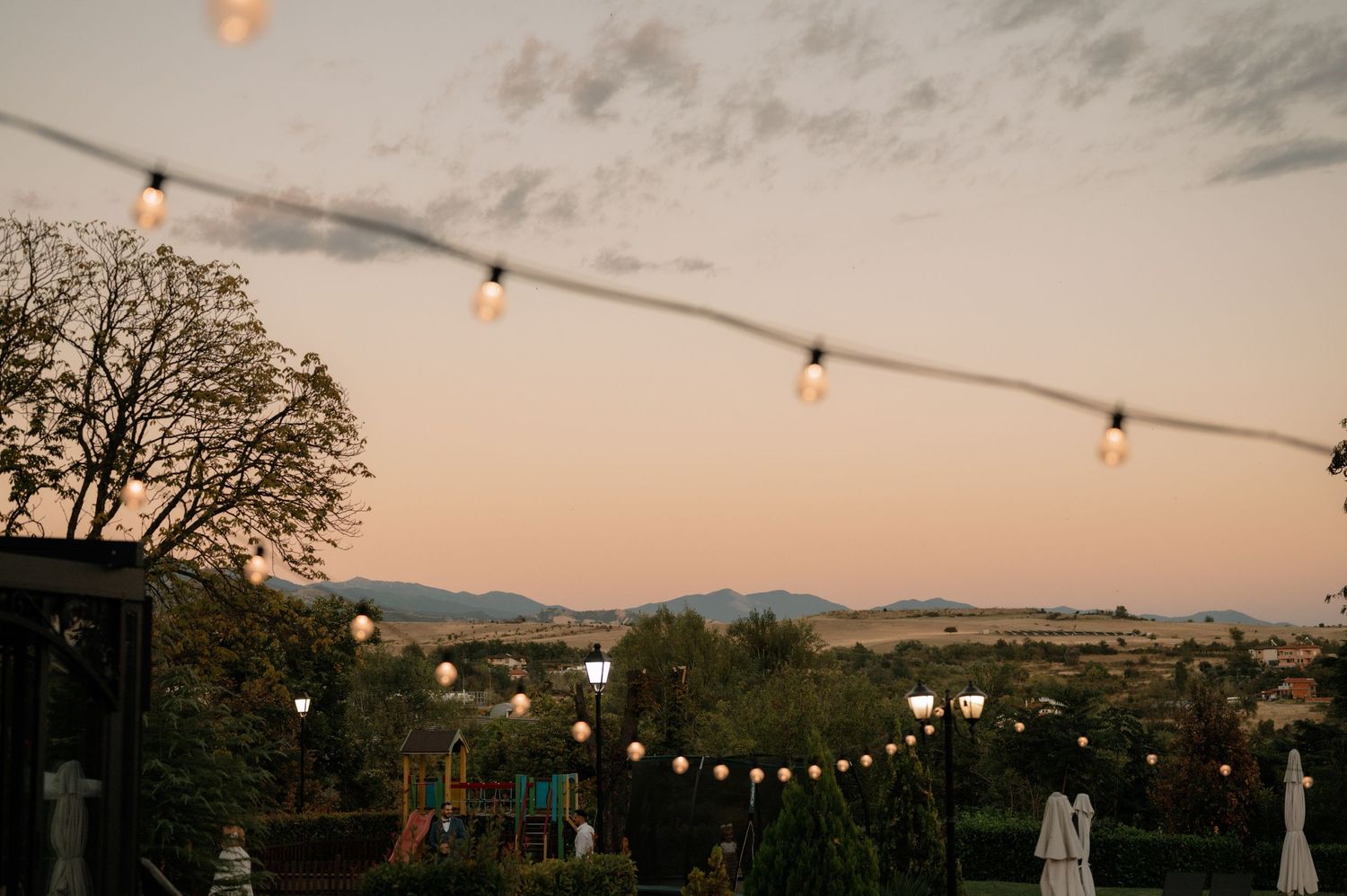 String lights illuminate an outdoor patio area at dusk with mountains visible in the background.