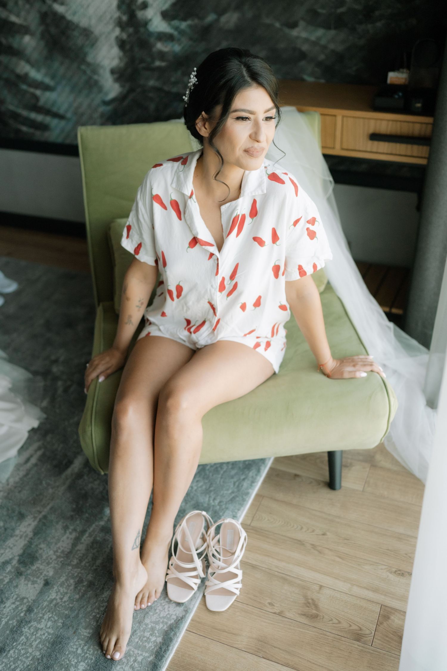 Person in white and red floral dress lounges on mint green chair with sandals on wooden floor.