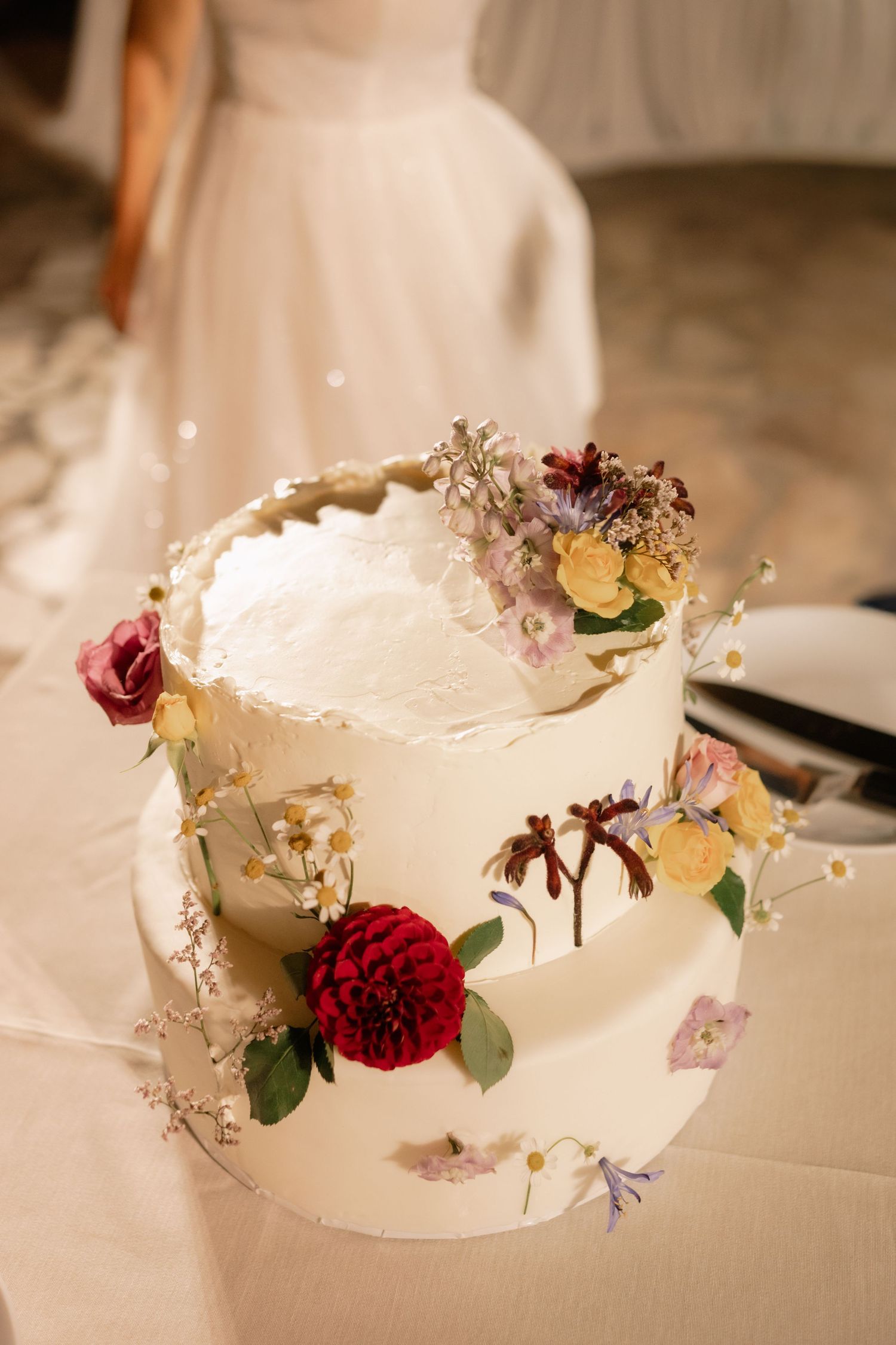 Elegant two-tier white wedding cake decorated with fresh red roses, yellow flowers and delicate floral accents.