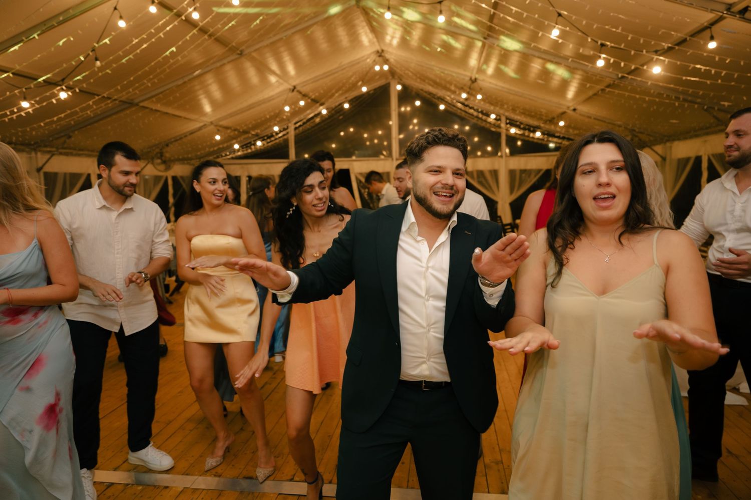 Wedding party dancing and celebrating in a rustic venue with string light decorations.