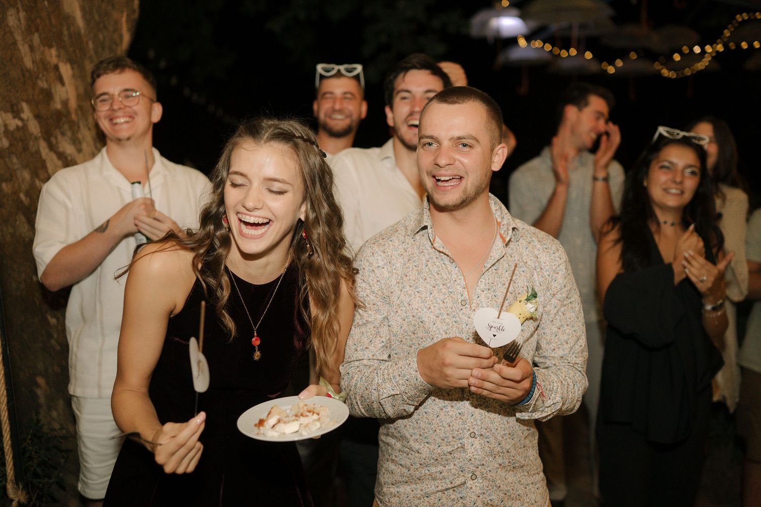 People dancing and celebrating at a lively nighttime party with twinkling lights in the background.