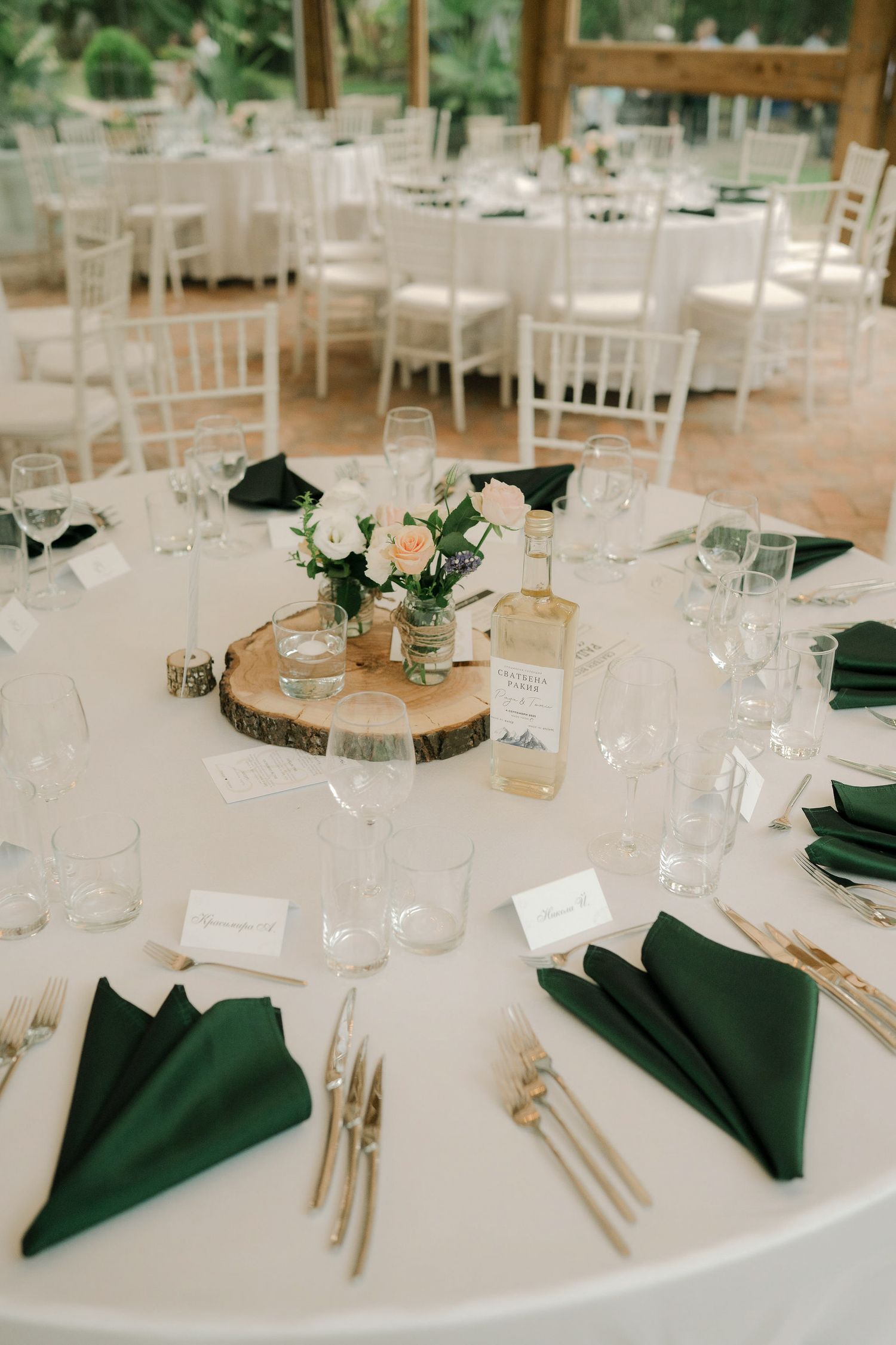 Elegant wedding table setting with white linens, forest green napkins, and rustic wood slice centerpiece with floral arrangement.