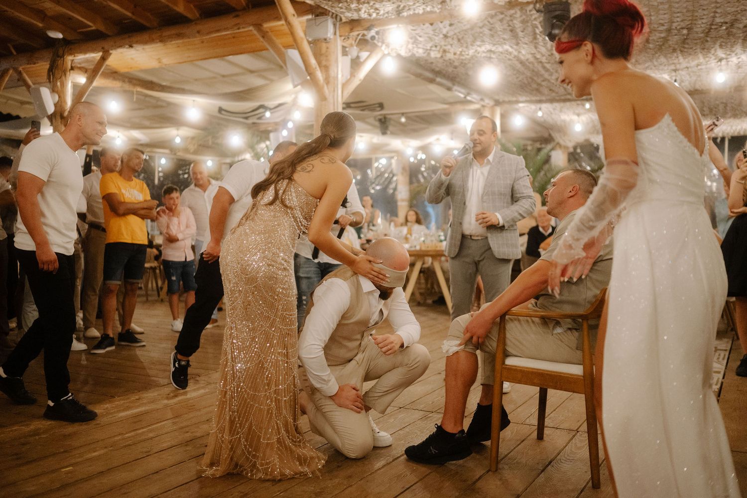 Vintage-style wedding reception in rustic barn venue with warm lighting and dancing guests on wooden floor.