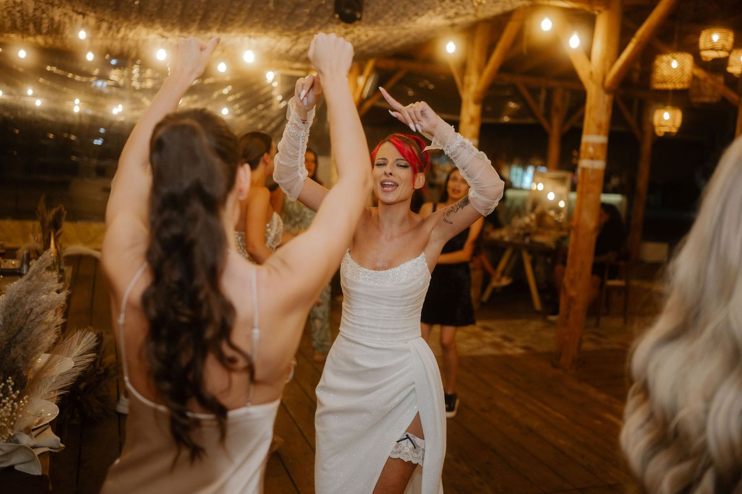 People dancing joyfully at a rustic barn wedding reception with string lights overhead.