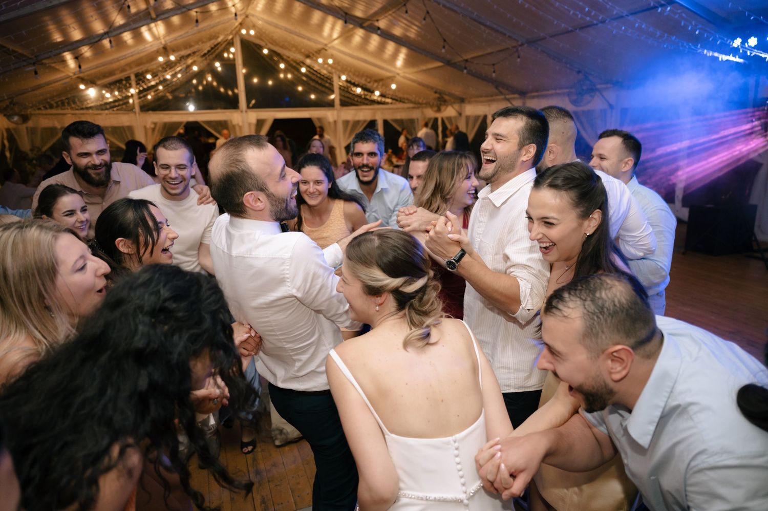 Wedding guests dance and celebrate together on a dimly lit dance floor decorated with string lights overhead.