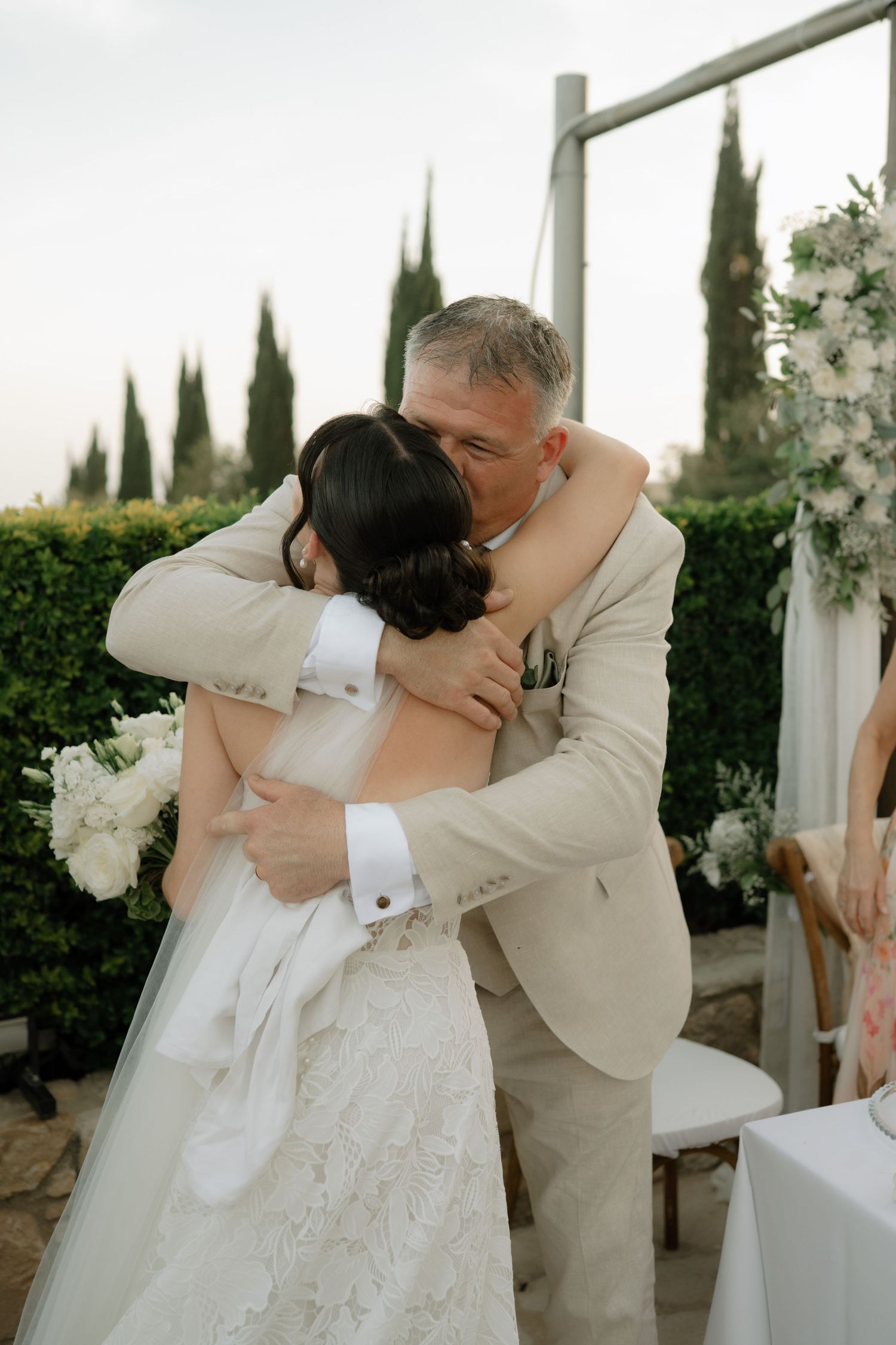 Father of the bride embracing his daughter in a heartfelt hug at an outdoor wedding ceremony.