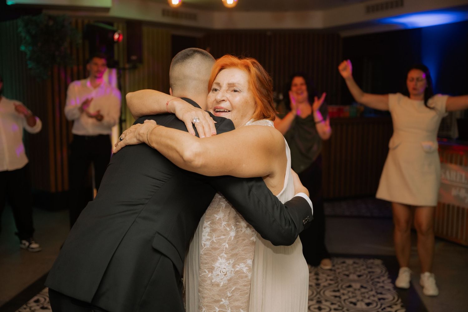 A couple shares an intimate dance moment at a wedding reception while other guests dance in the background.