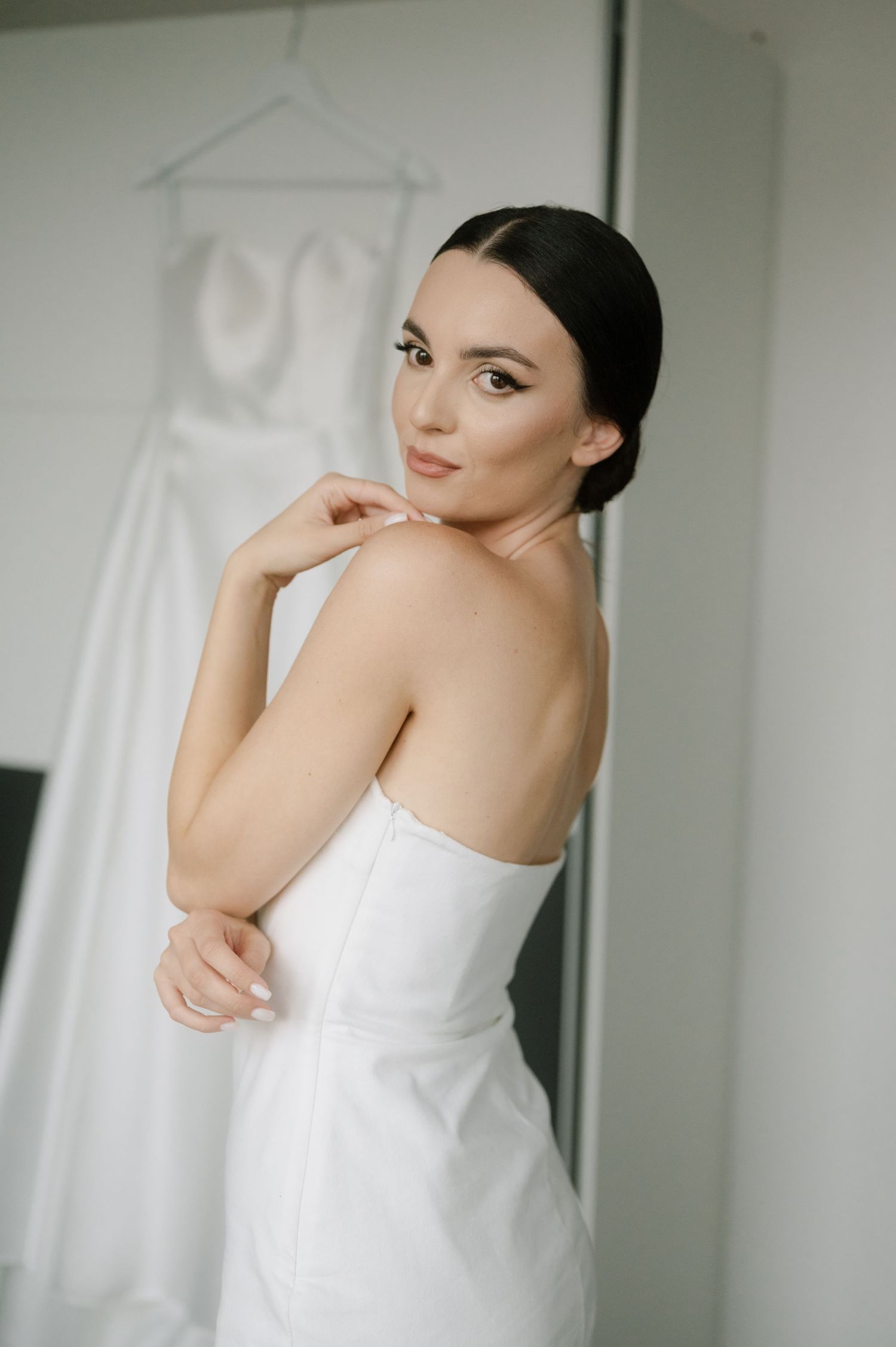 A person in a white sleeveless top poses gracefully against a bright minimalist background in an artistic portrait series.