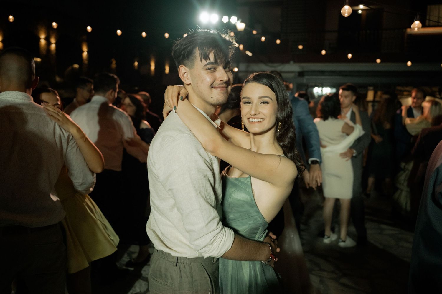 Wedding guests dance together on a dimly lit dance floor during an evening celebration.