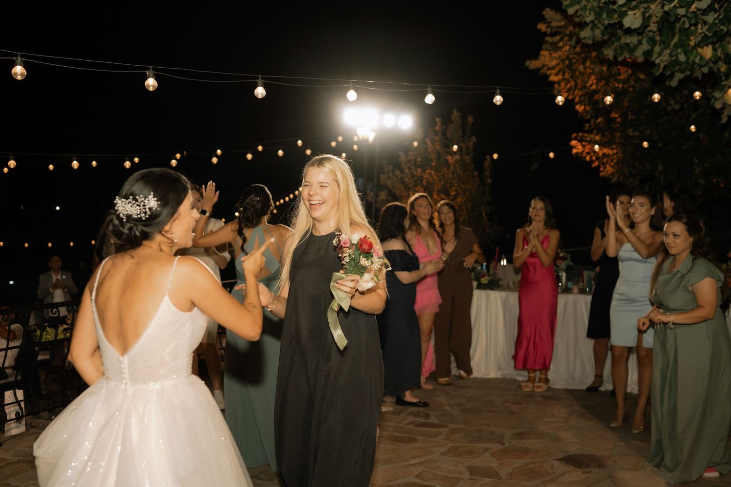 A wedding couple dances under twinkling string lights at an outdoor evening reception.