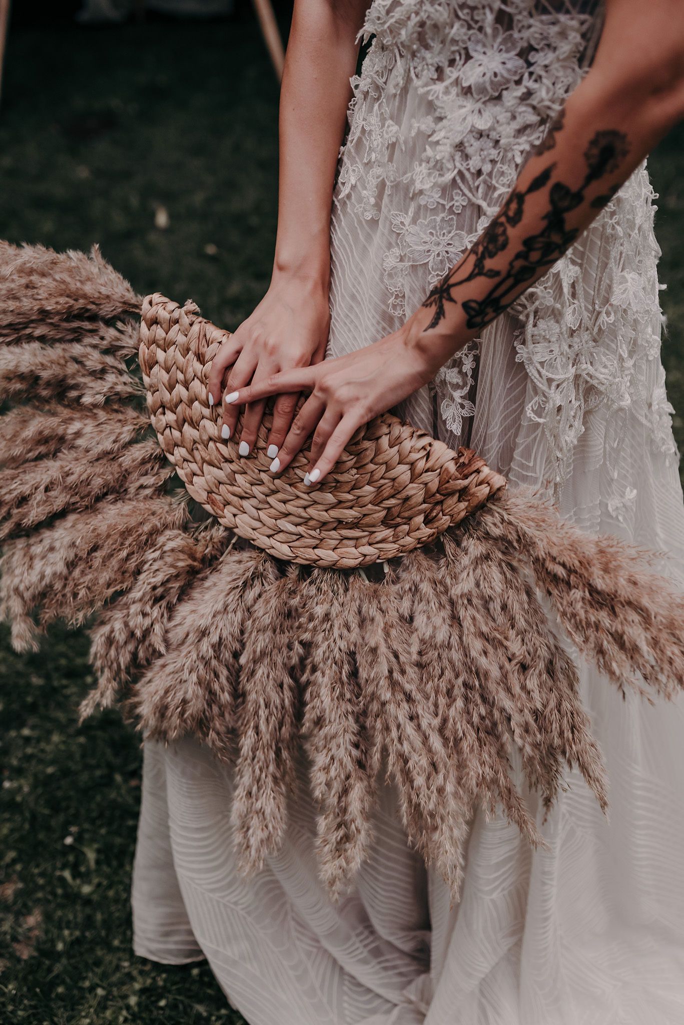 Hands delicately arranging dried pampas grass against a white lace wedding dress.