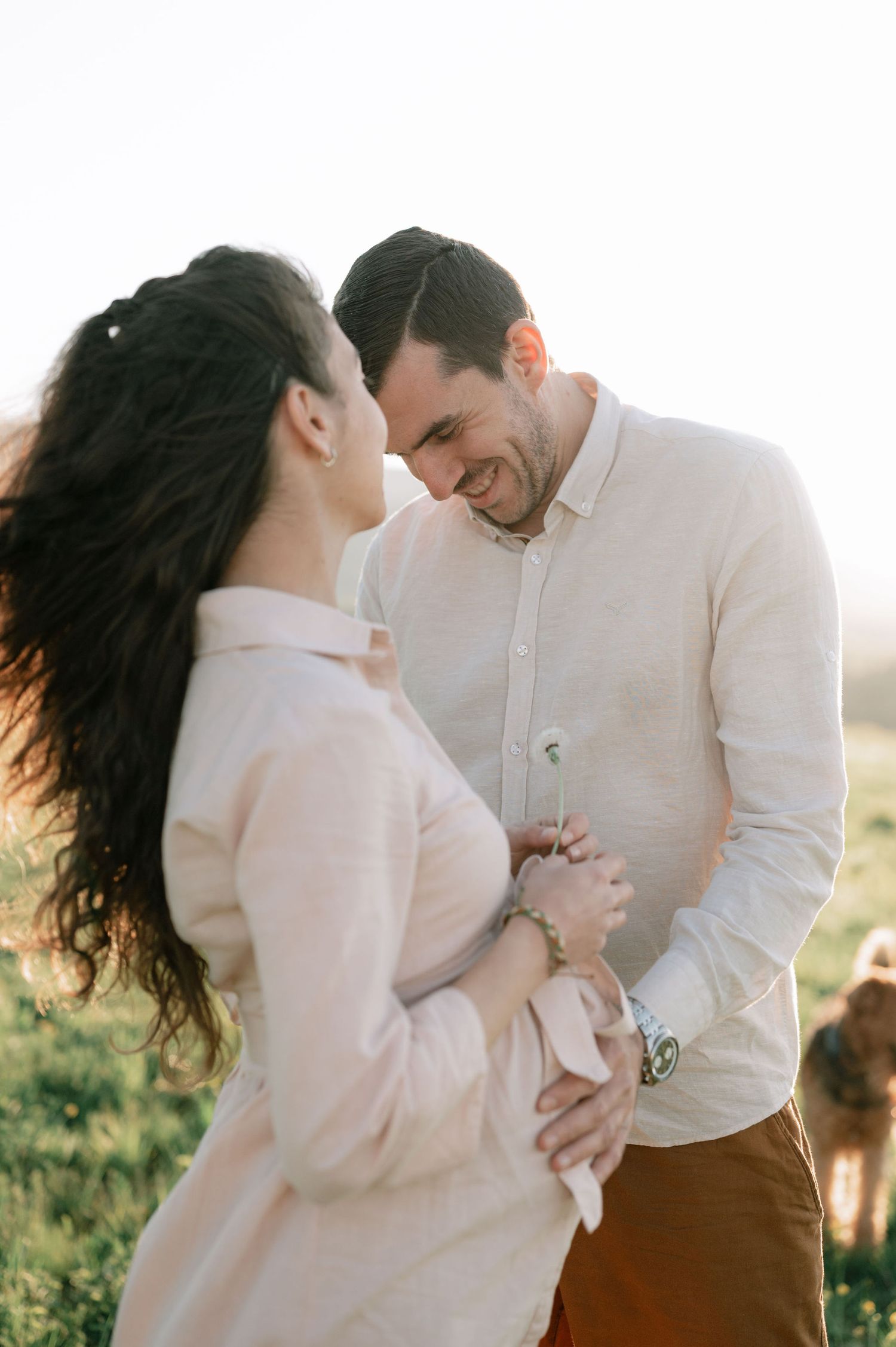 A romantic couple shares an intimate moment while laughing together during golden hour in a sunlit outdoor setting.