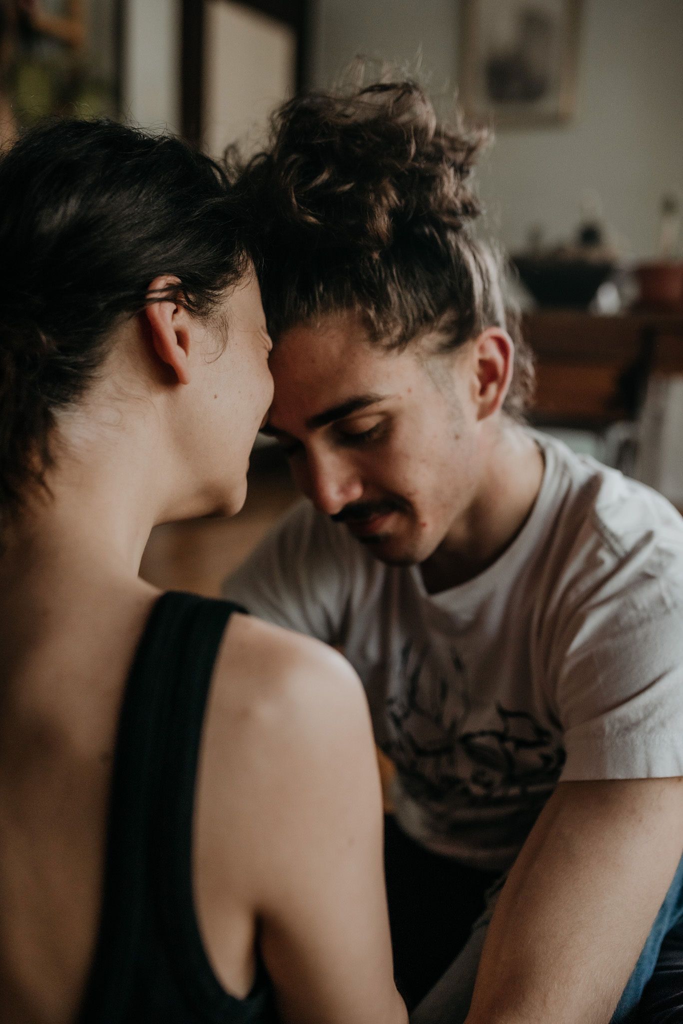 An intimate couple shares a tender moment together in a dimly lit room with soft natural lighting.