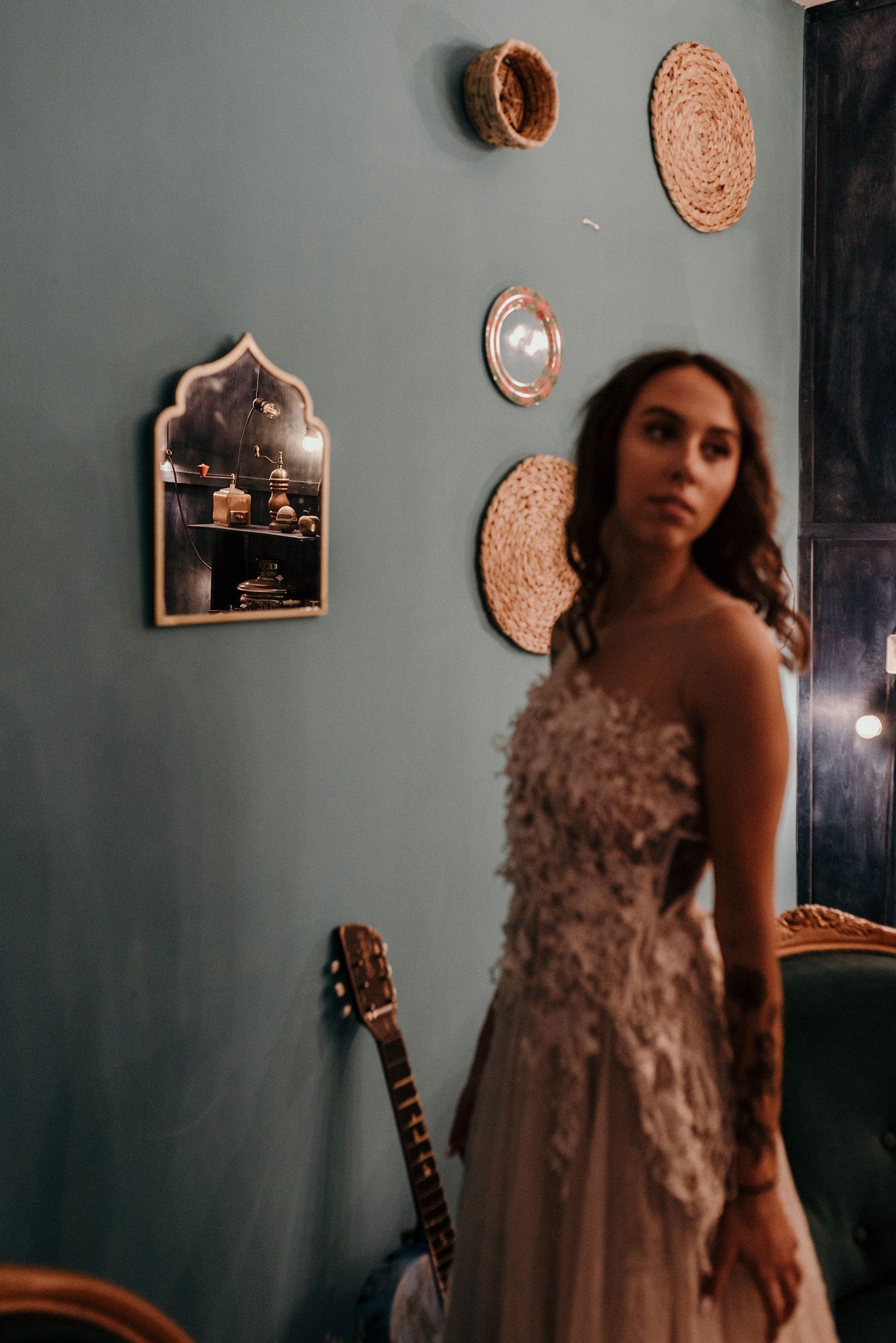 Elegant wedding dress photographed against sage green walls with decorative copper accents and a guitar.