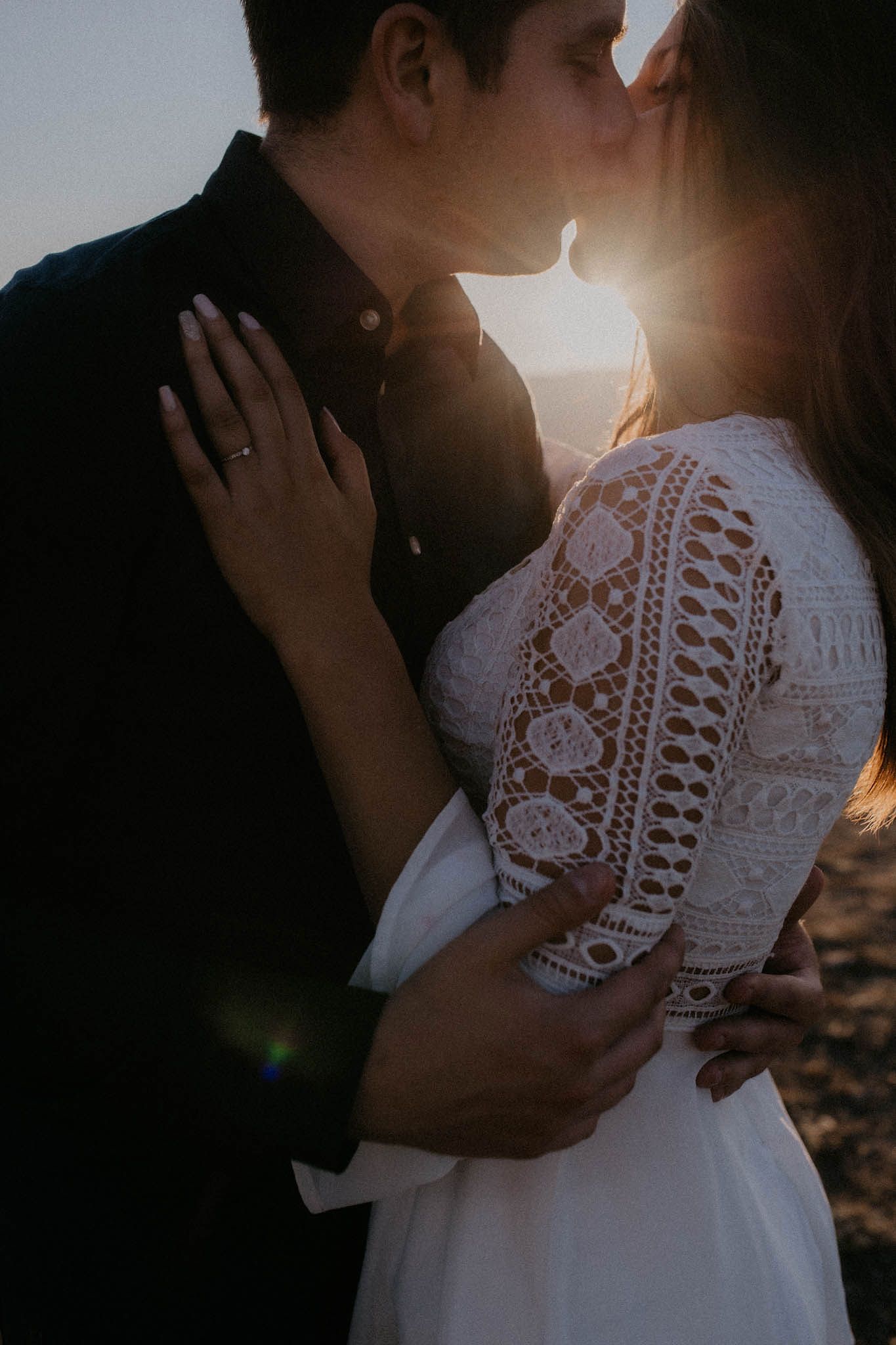 Romantic sunset moment captured between couple with sunflare and lace dress details.