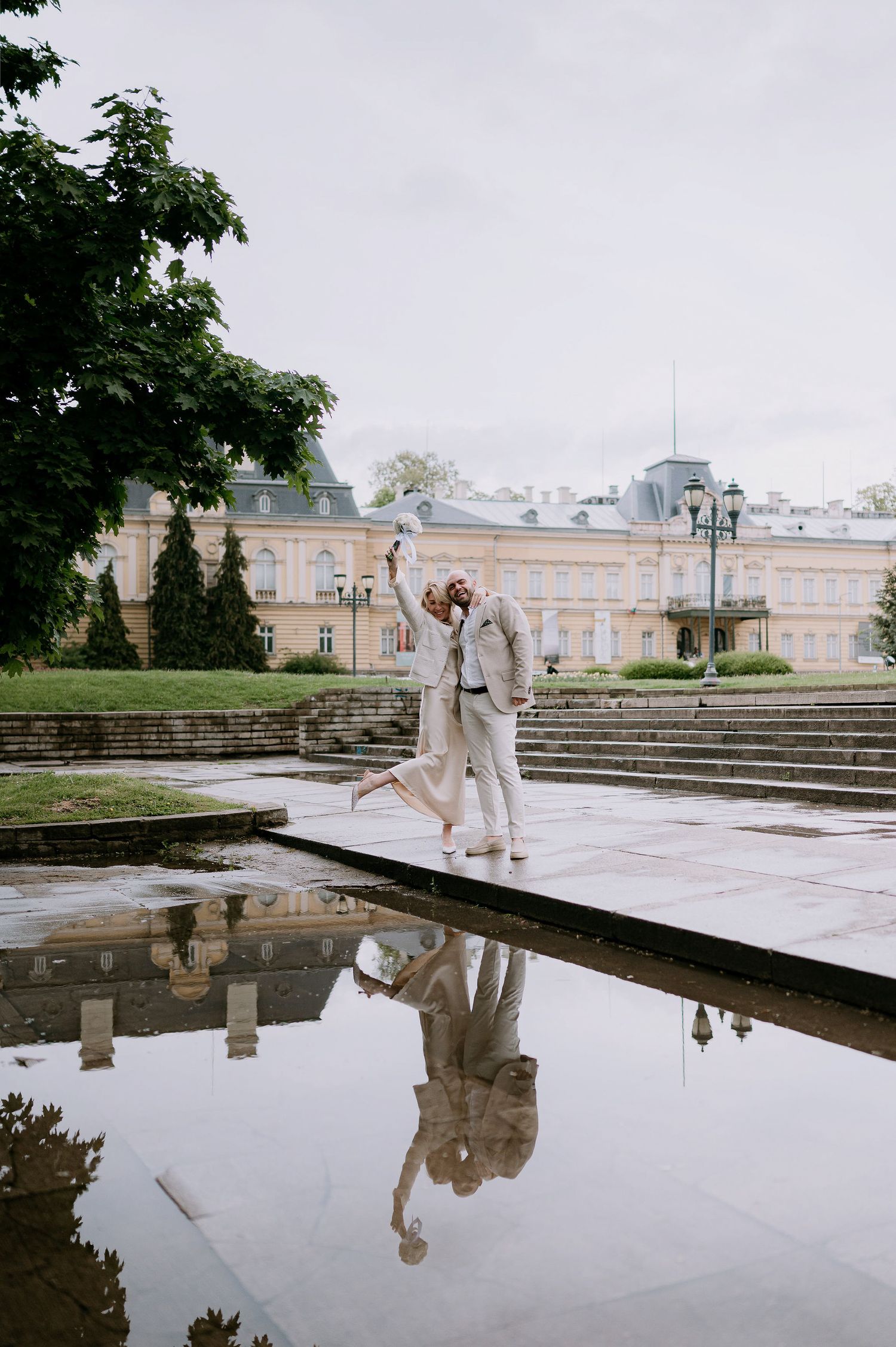 Dancing figures create reflections in courtyard pool with classical architecture in soft overcast light.