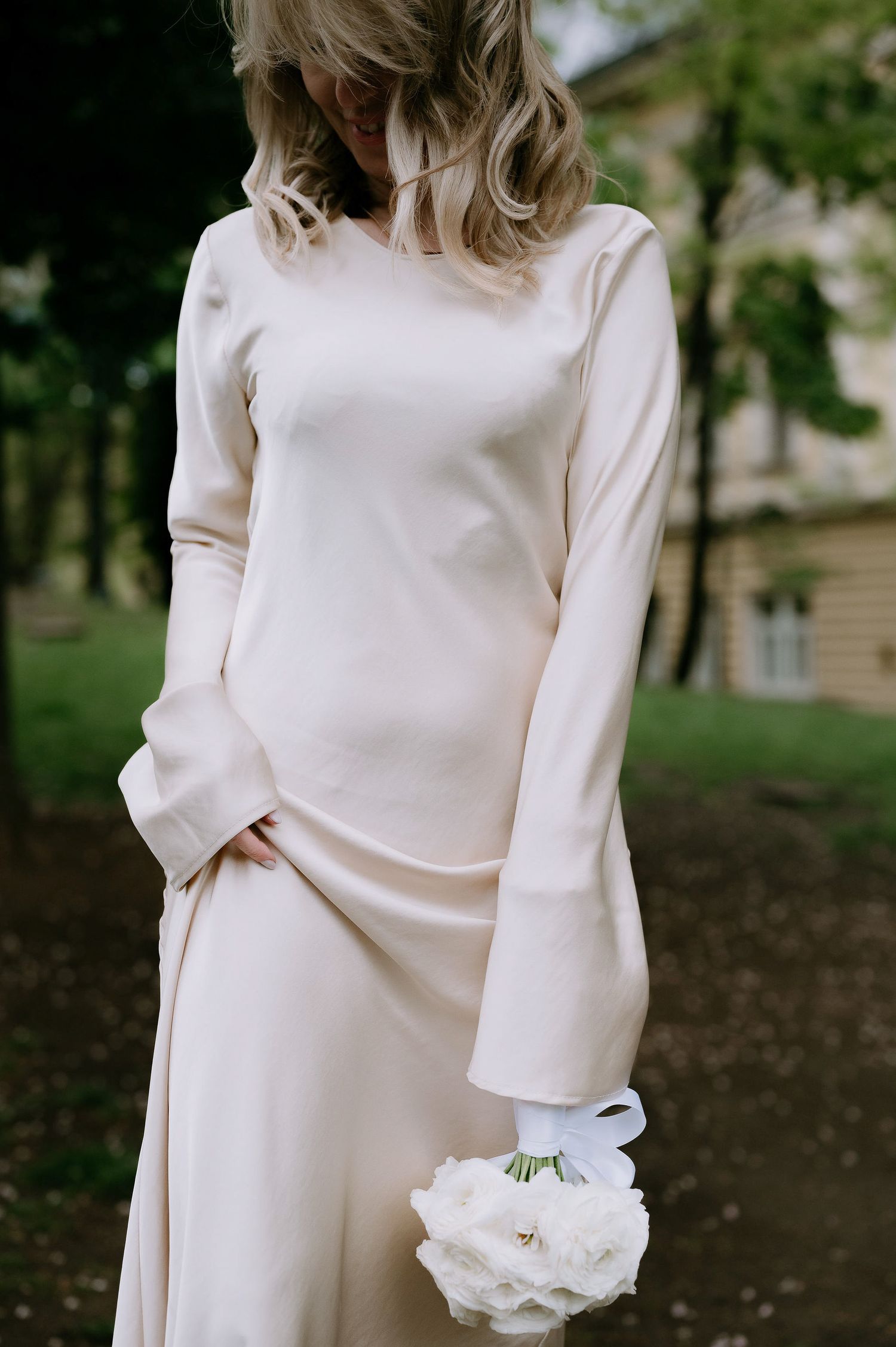 Minimalist white wedding dress with long sleeves shown against a natural outdoor backdrop.
