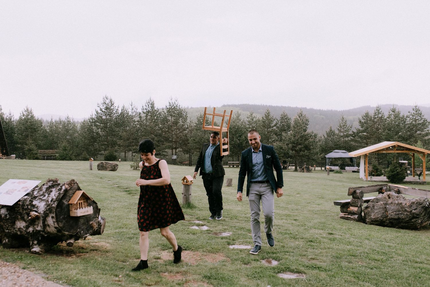 Wedding guests walking and dancing on a grassy field with mountains and pine trees in the background.