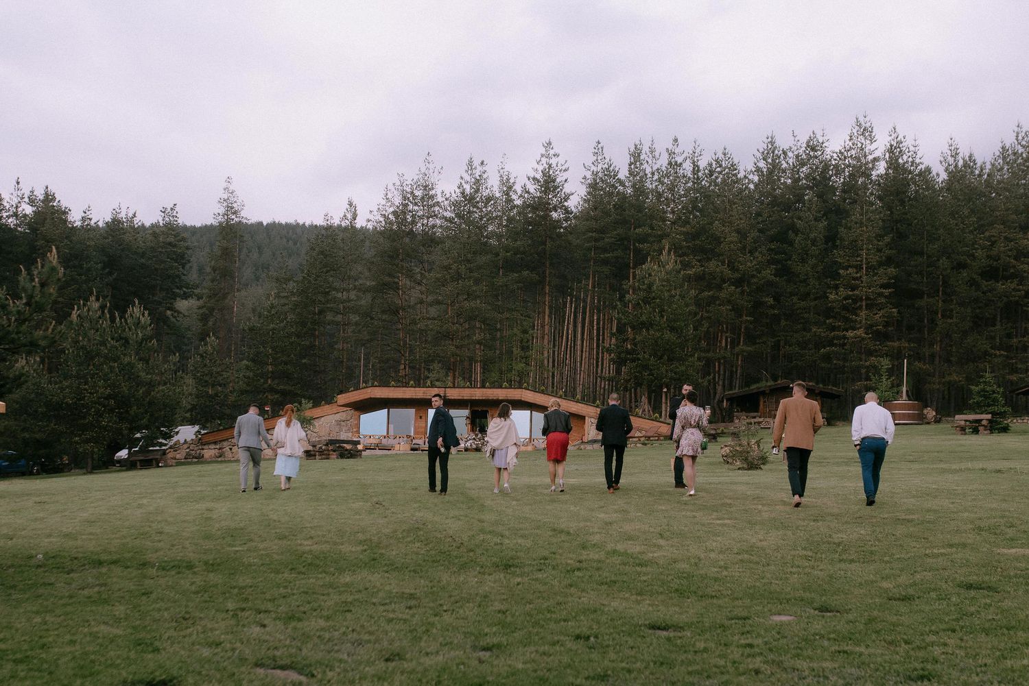 People walking across a grassy field with evergreen trees in the background.