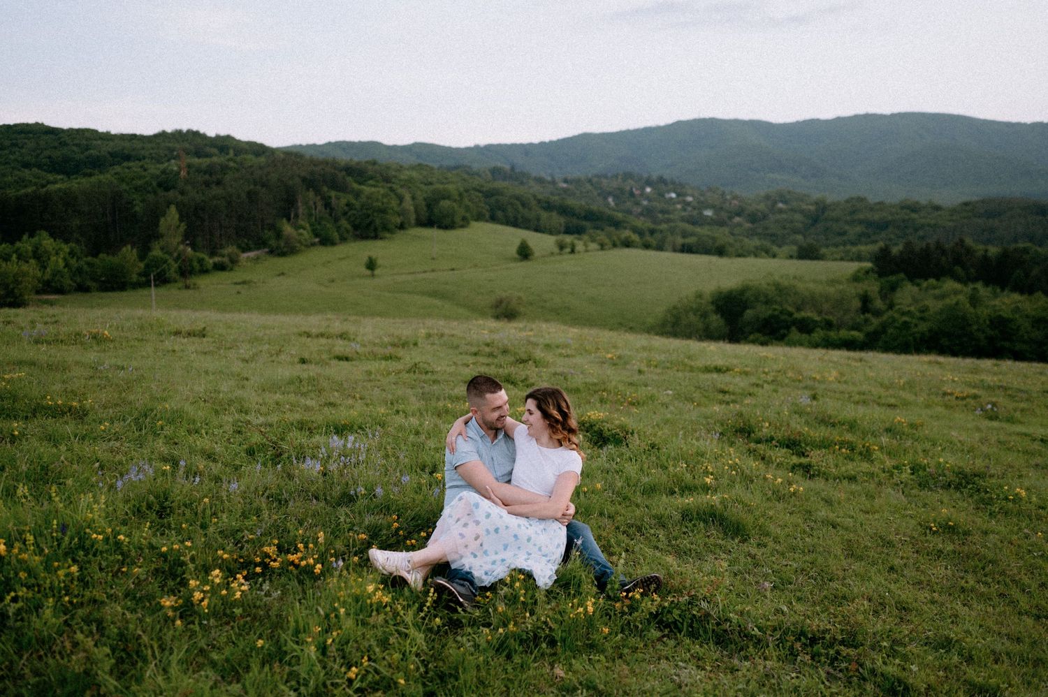 A couple relaxes in a scenic mountain meadow filled with yellow wildflowers at dusk.